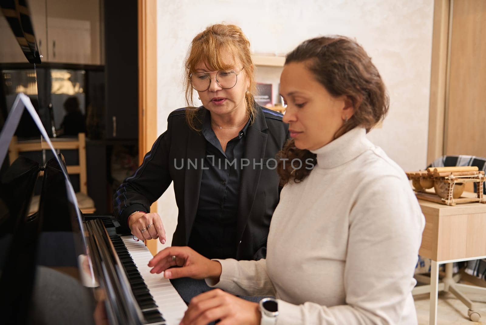 Young adult Asian female pianist, music teacher teaching piano and music lesson to a woman by artgf