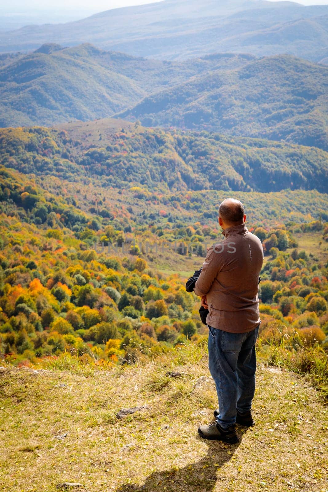 From a sacred peak overlook, a man takes in the tranquil mountain scenery, marveling at the breathtaking view. The serene ambiance and untouched natural beauty create a sense of wonder and inner calm.