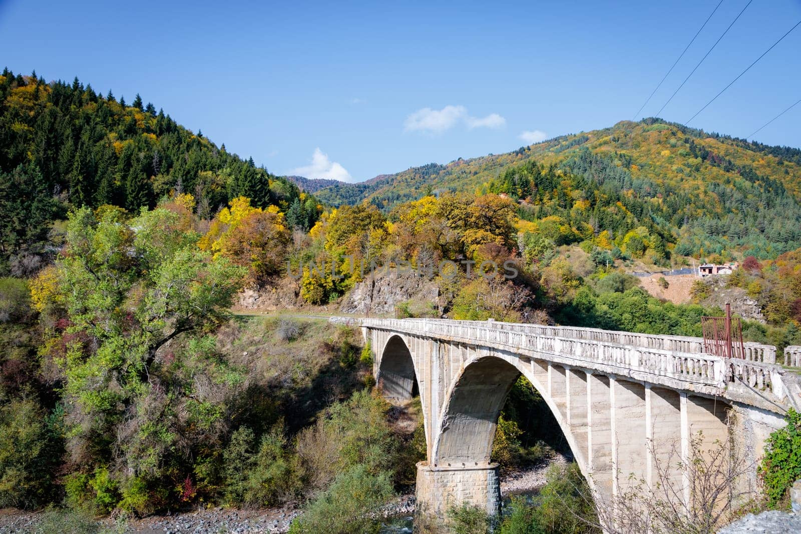 A stunning tall bridge spans over a serene river nestled in the midst of towering mountains. The impressive structure offers a captivating view of the natural landscape.
