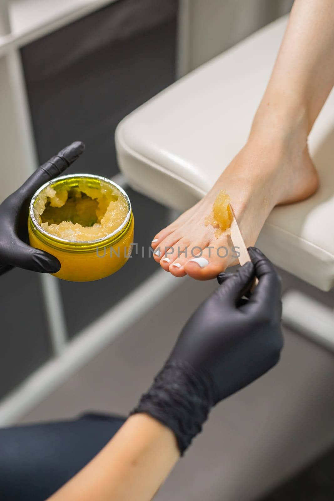 Woman doing foot peeling in pedicure SPA salon. Sugar scrub and relax beauty procedure.