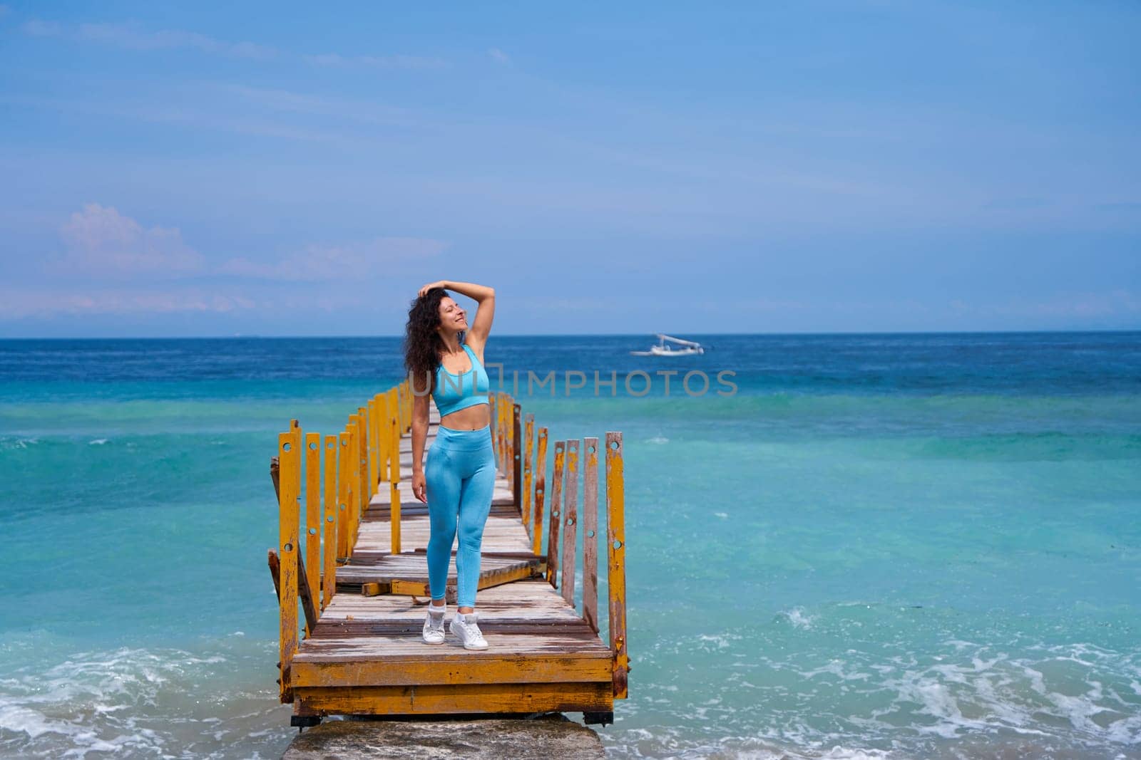 A slender young woman walks along an old wooden pier, which goes into the horizon of the incredible azure color of the ocean. by Try_my_best