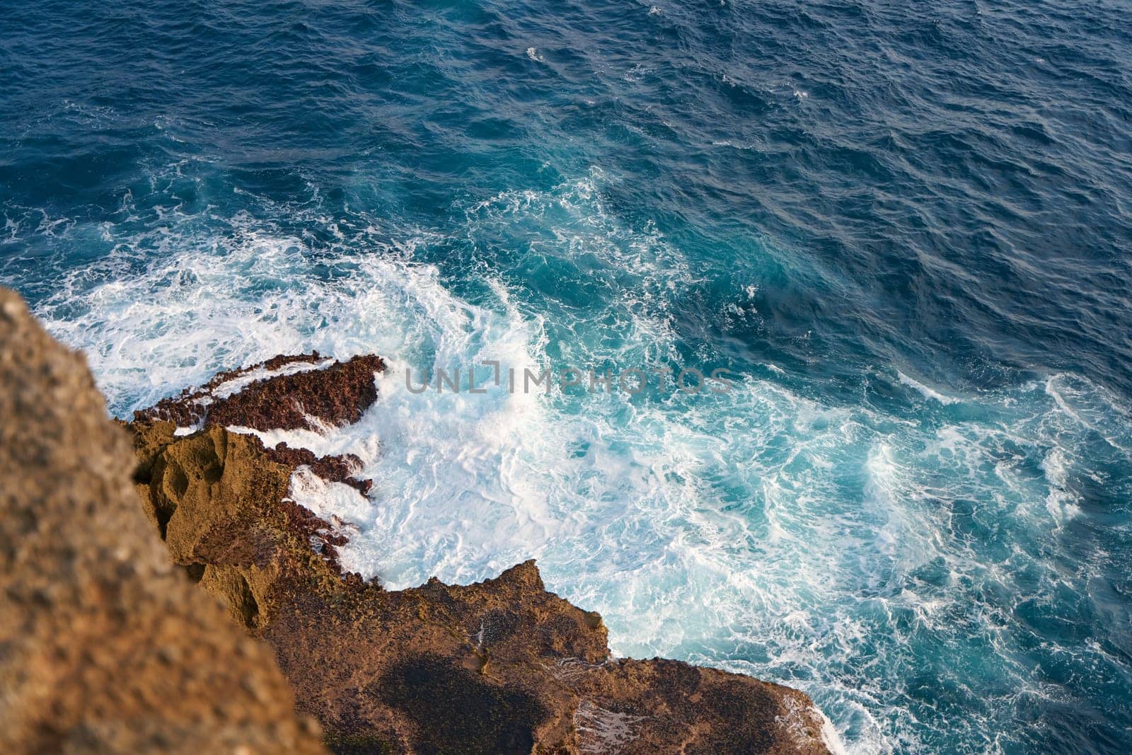 An ocean wave crashing against a textured rock at sunset