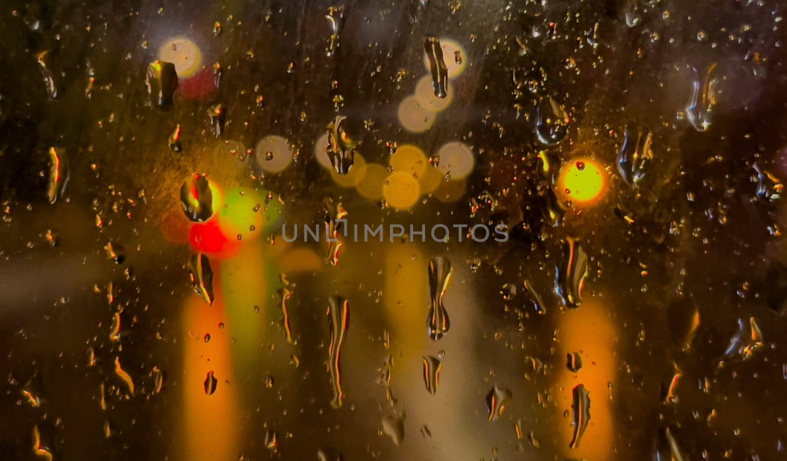 Rain bokeh road lights. Abstract shot of evening city traffic bokeh. Multicolored lights of the evening city and passing cars through a wet rainy window