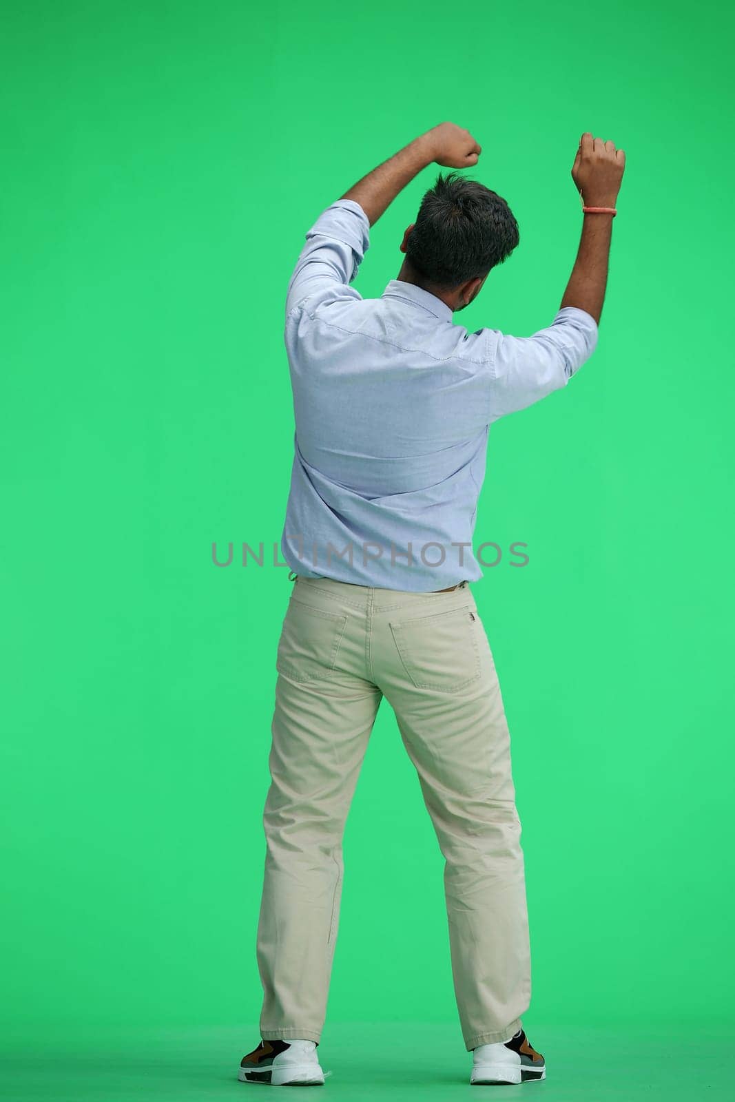 A man in a blue shirt, on a green background, standing tall, waving his arms, back view.