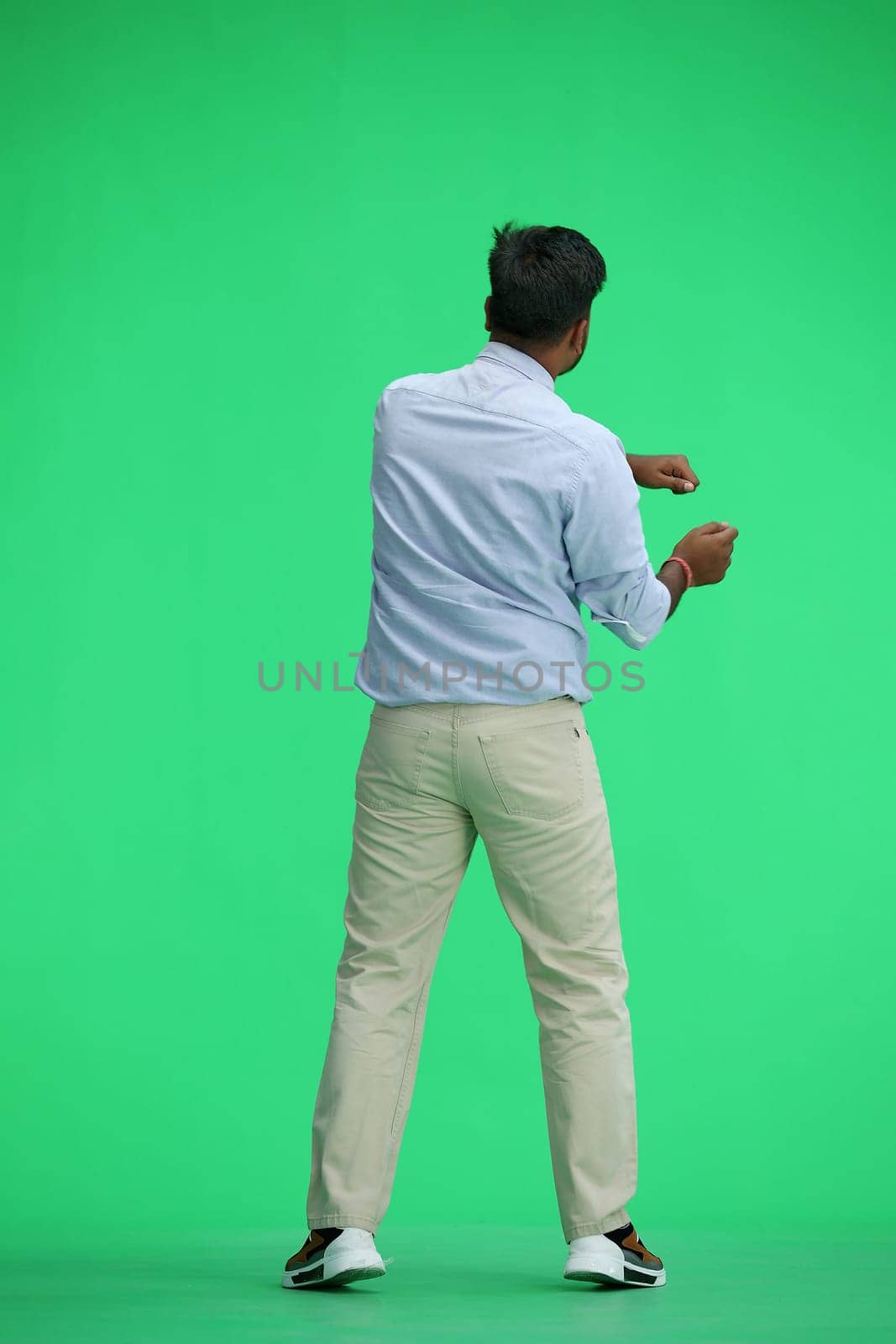 A man in a blue shirt, on a green background, standing tall, waving his arms, back view by Prosto