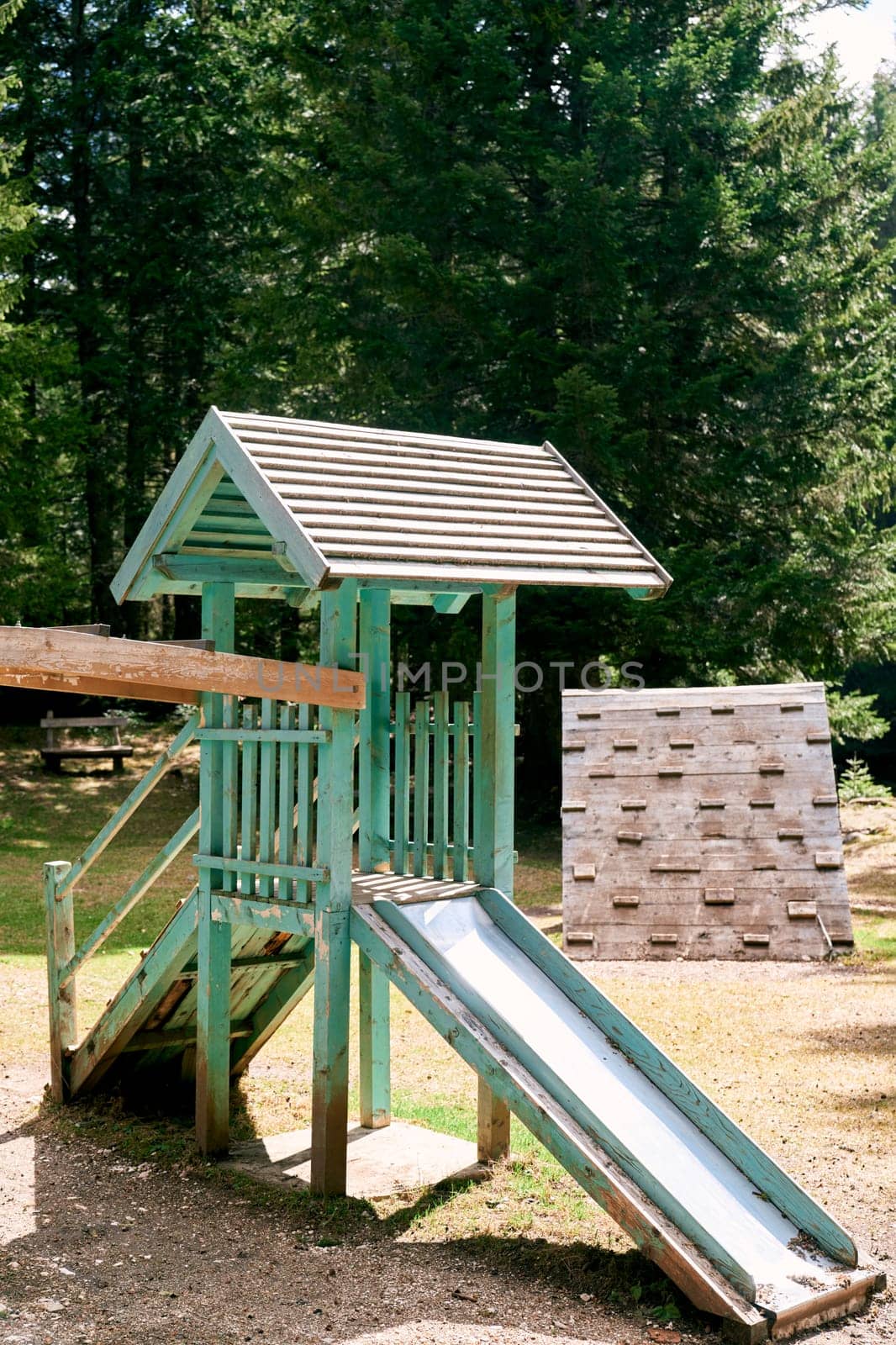 Wooden house with a slide on a playground in the forest next to a climbing wall. High quality photo