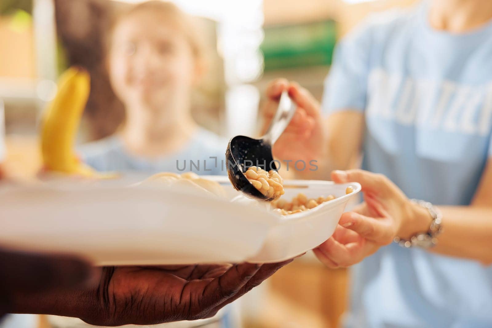 Photo focus on caucasian woman serving baked beans to hungry underprivileged african american person at a non-profit food drive. Close-up shot of free food distribution by humanitarian aid team.