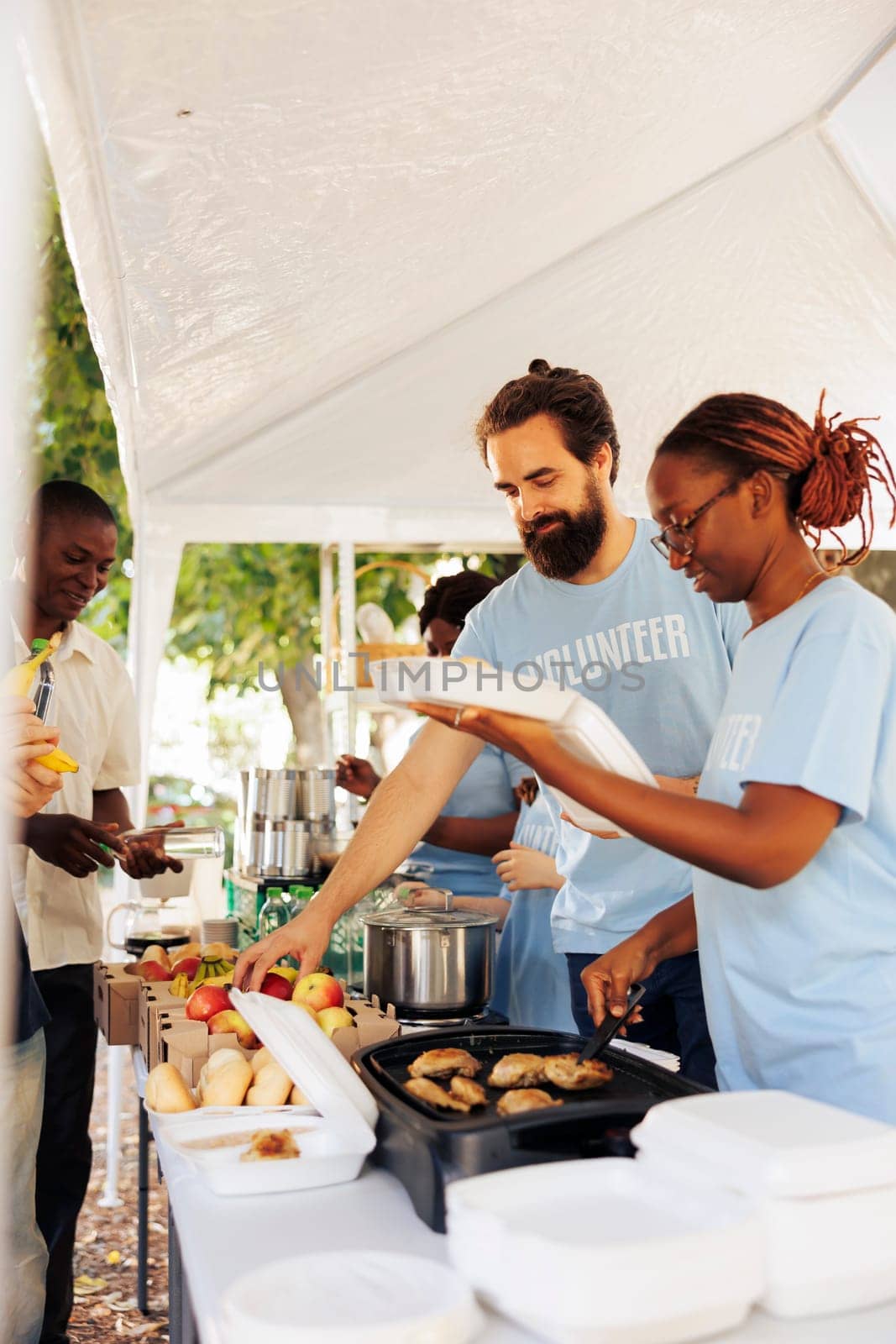 Young black woman and caucasian man cook and donate free meal at a food drive to the poor and needy. Charity workers helping homeless people, supporting hunger relief, and combating poverty.