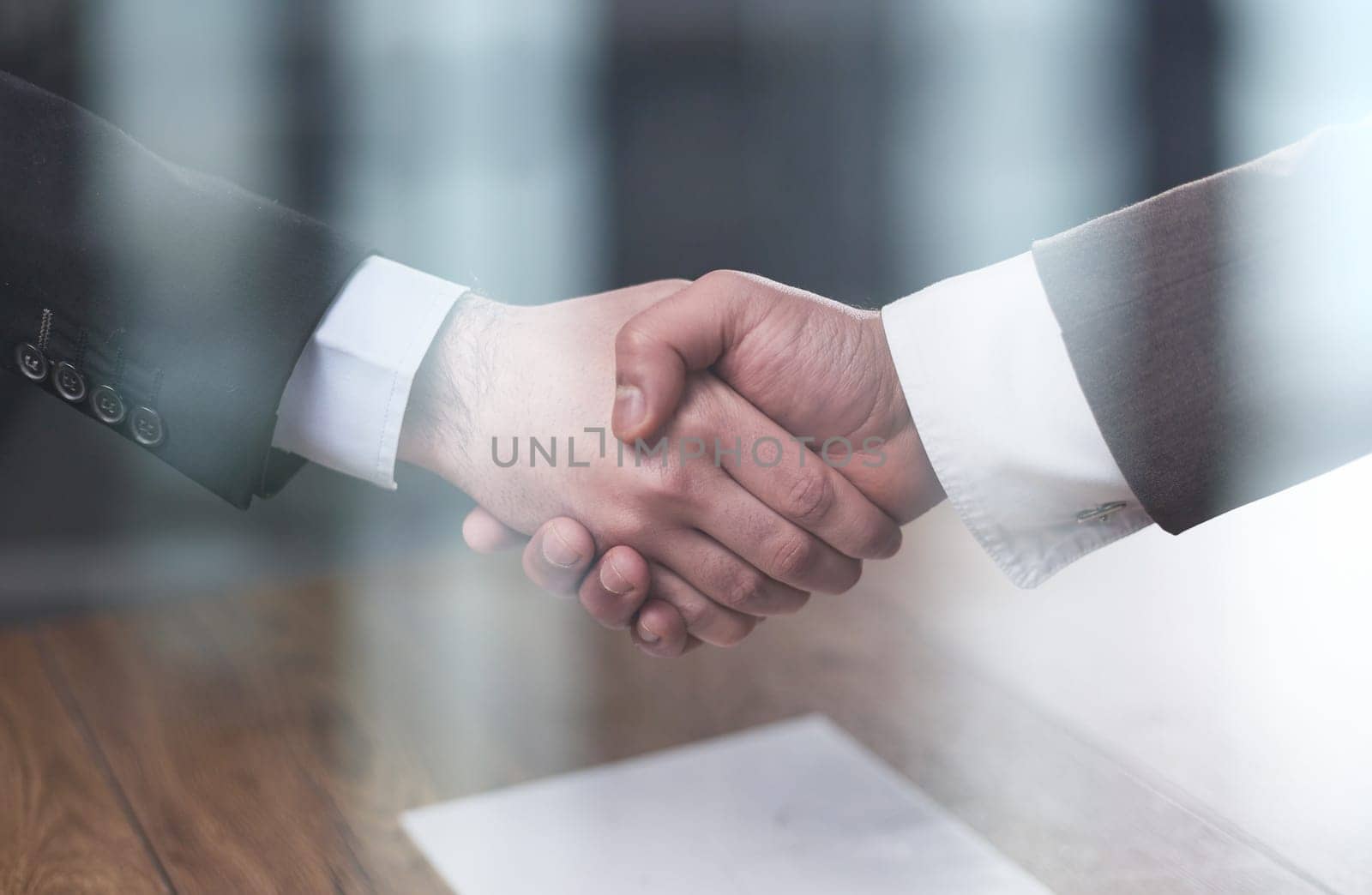 Closeup of hands of two young and successful male business people shaking hands over wooden table