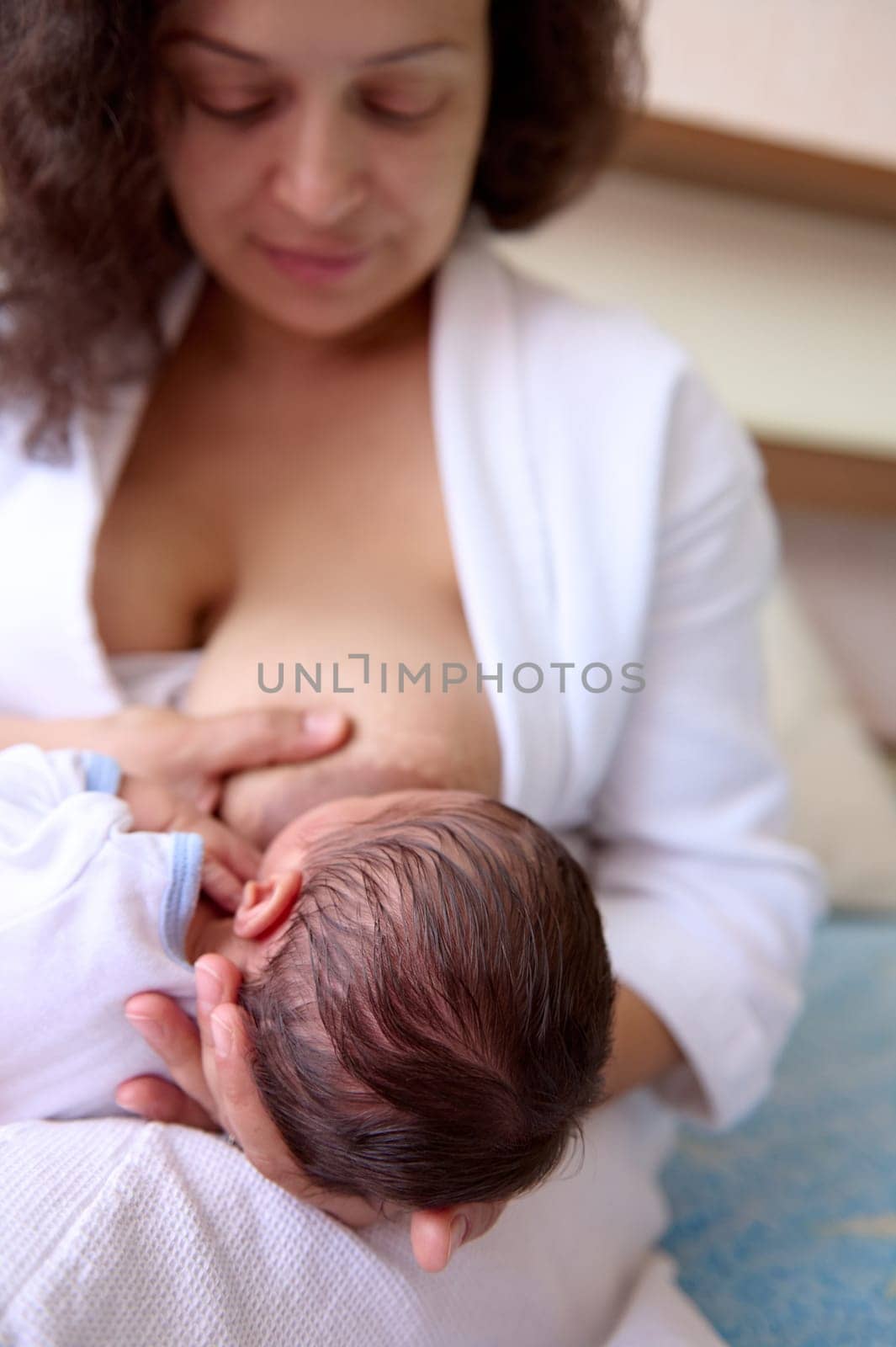 Beautiful happy loving young mother smiles while connects with her newborn baby, holds him in her arms, breastfeeds him by artgf