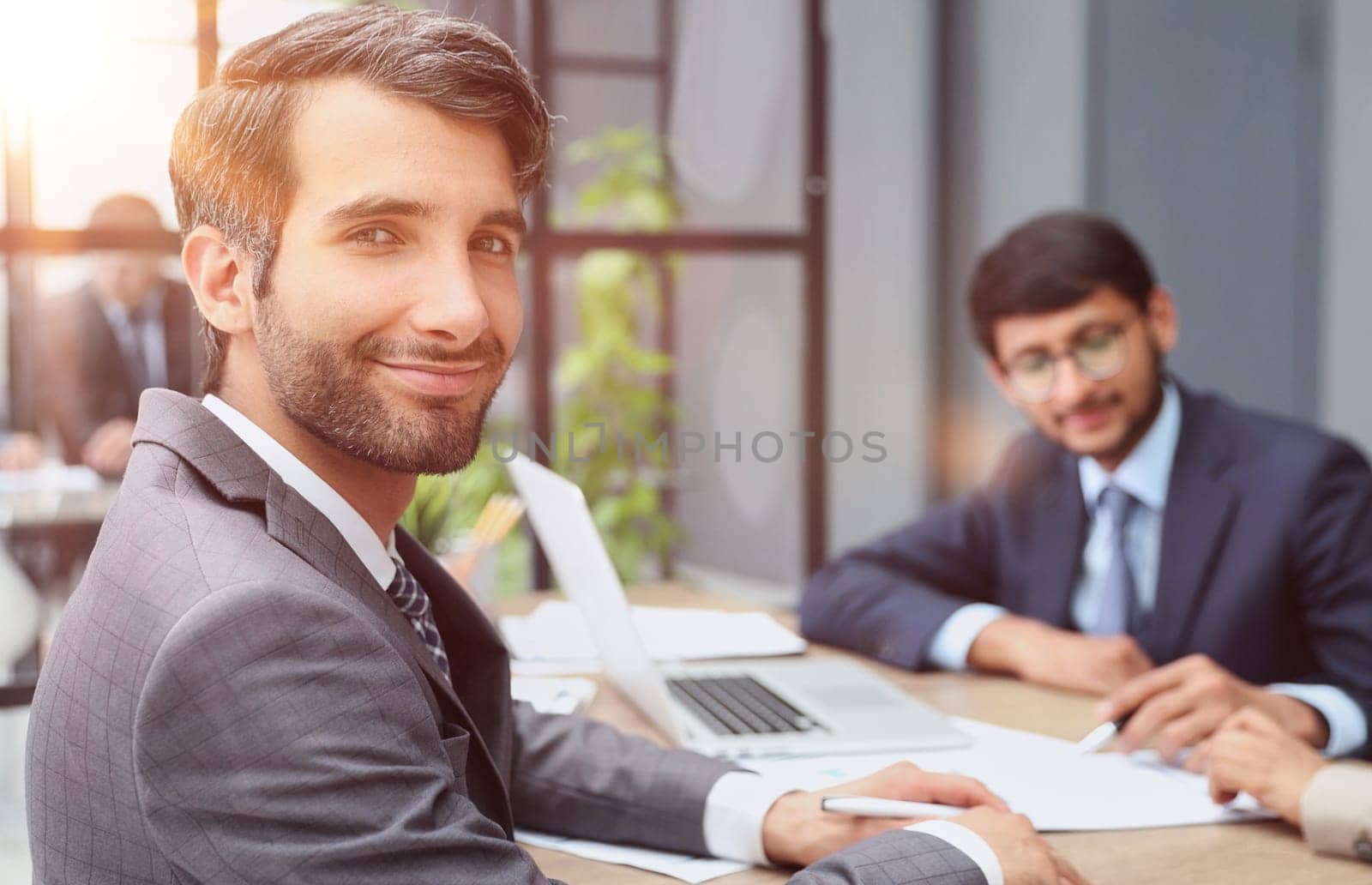 male boss against the background of her colleagues looks at the camera in a modern office by Prosto