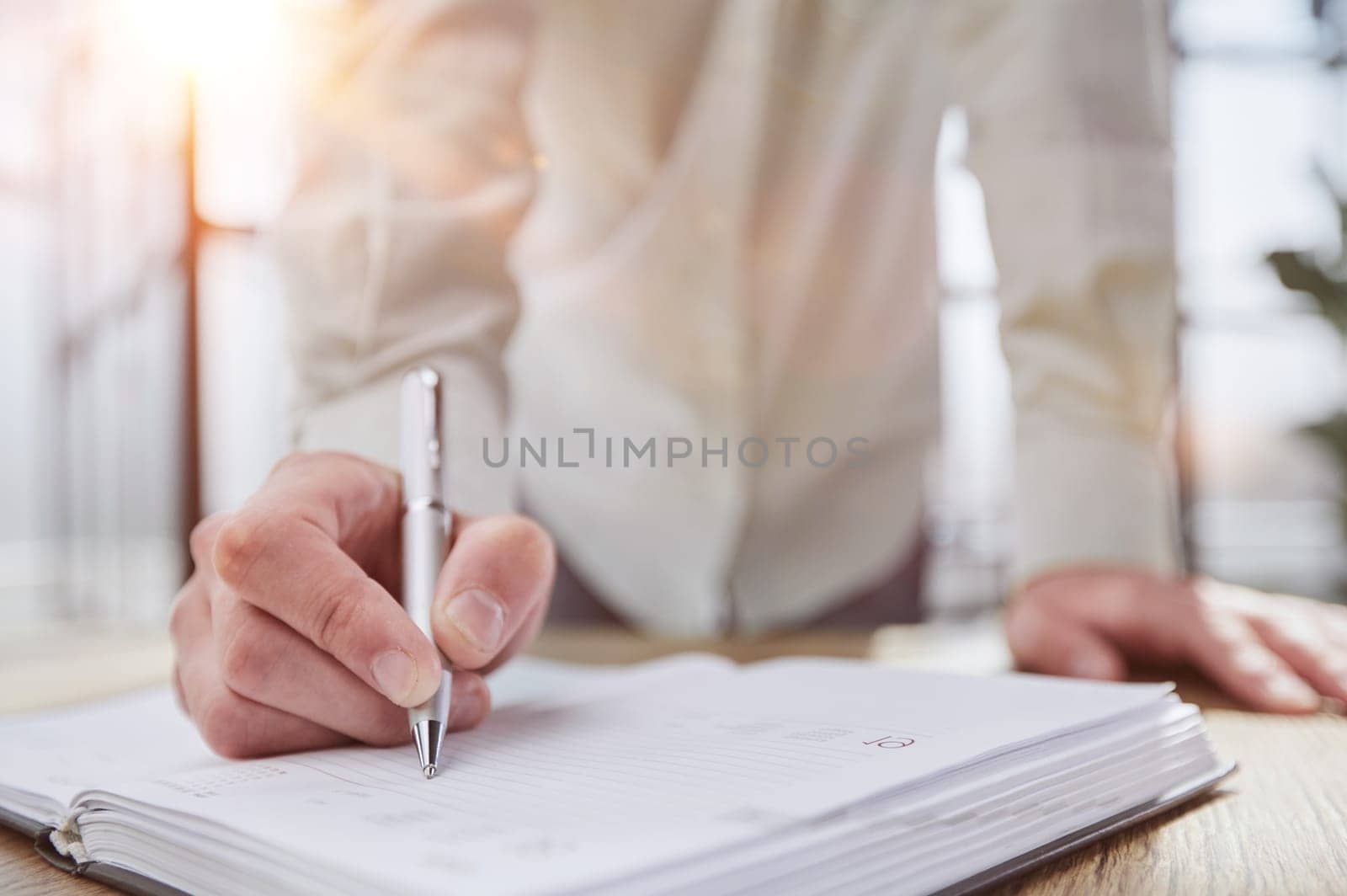 Businessman writes with a pen in diary sunny office, business and education concept. Close up by Prosto