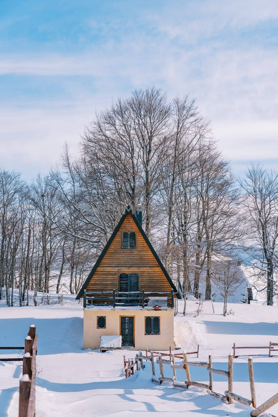 Triangular two-story house with a terrace behind a wooden fence in the snow. High quality photo