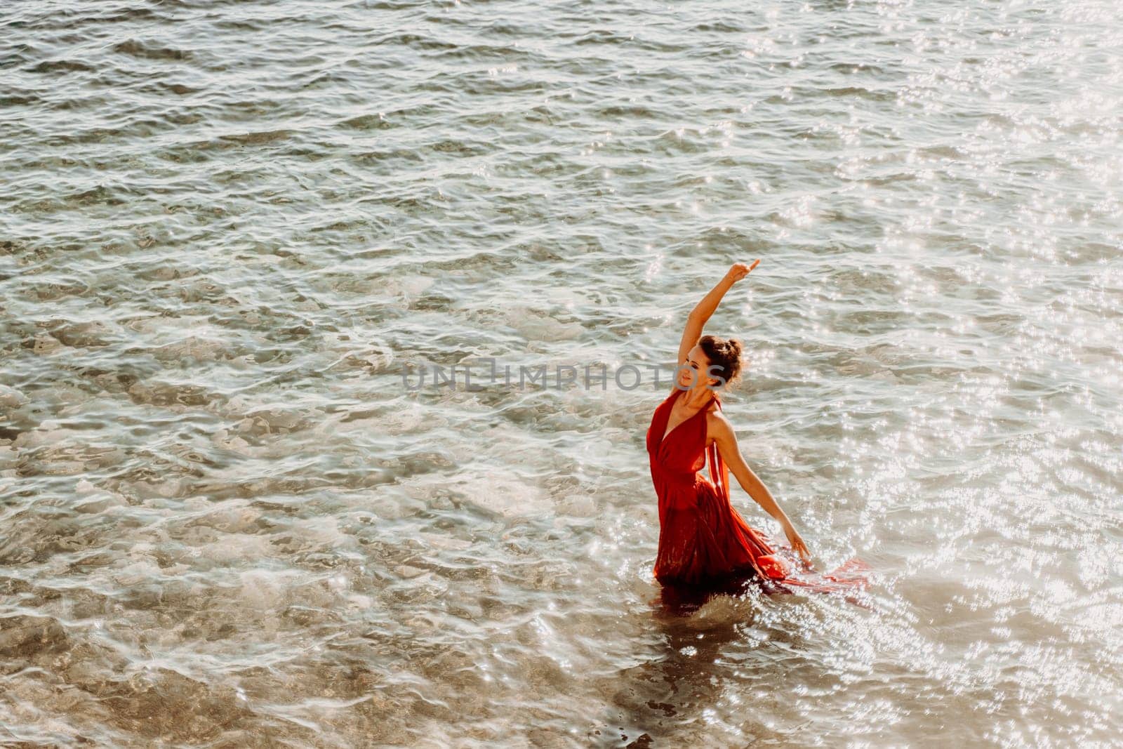 Woman red dress sea. Female dancer in a long red dress posing on a beach with rocks on sunny day.