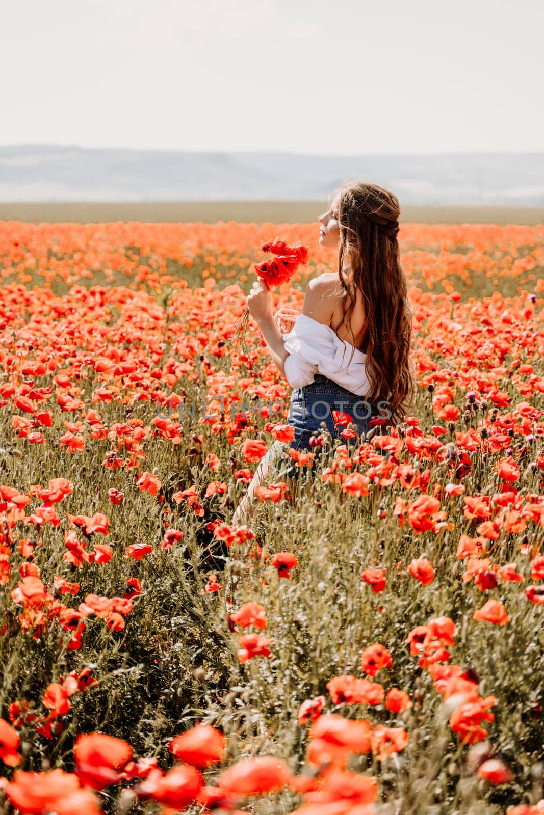 Woman poppies field. Side view of a happy woman with long hair in a poppy field and enjoying the beauty of nature in a warm summer day. by Matiunina