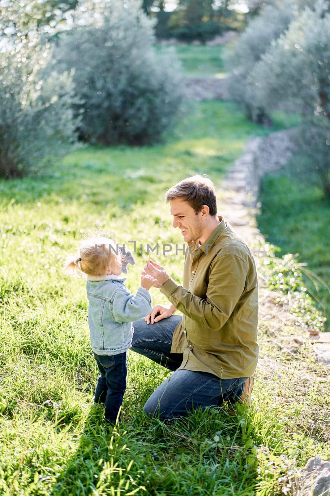 Dad is squatting near a little girl with a dandelion in his hand in a clearing. High quality photo