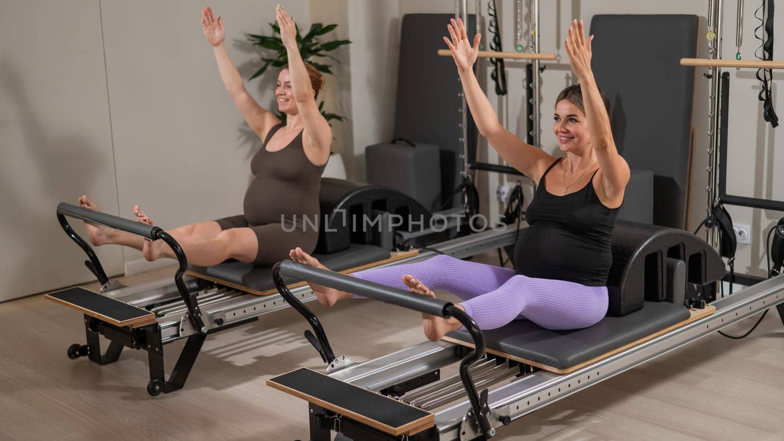 Two pregnant women do Pilates exercises on a reformer. Yoga class for pregnant women