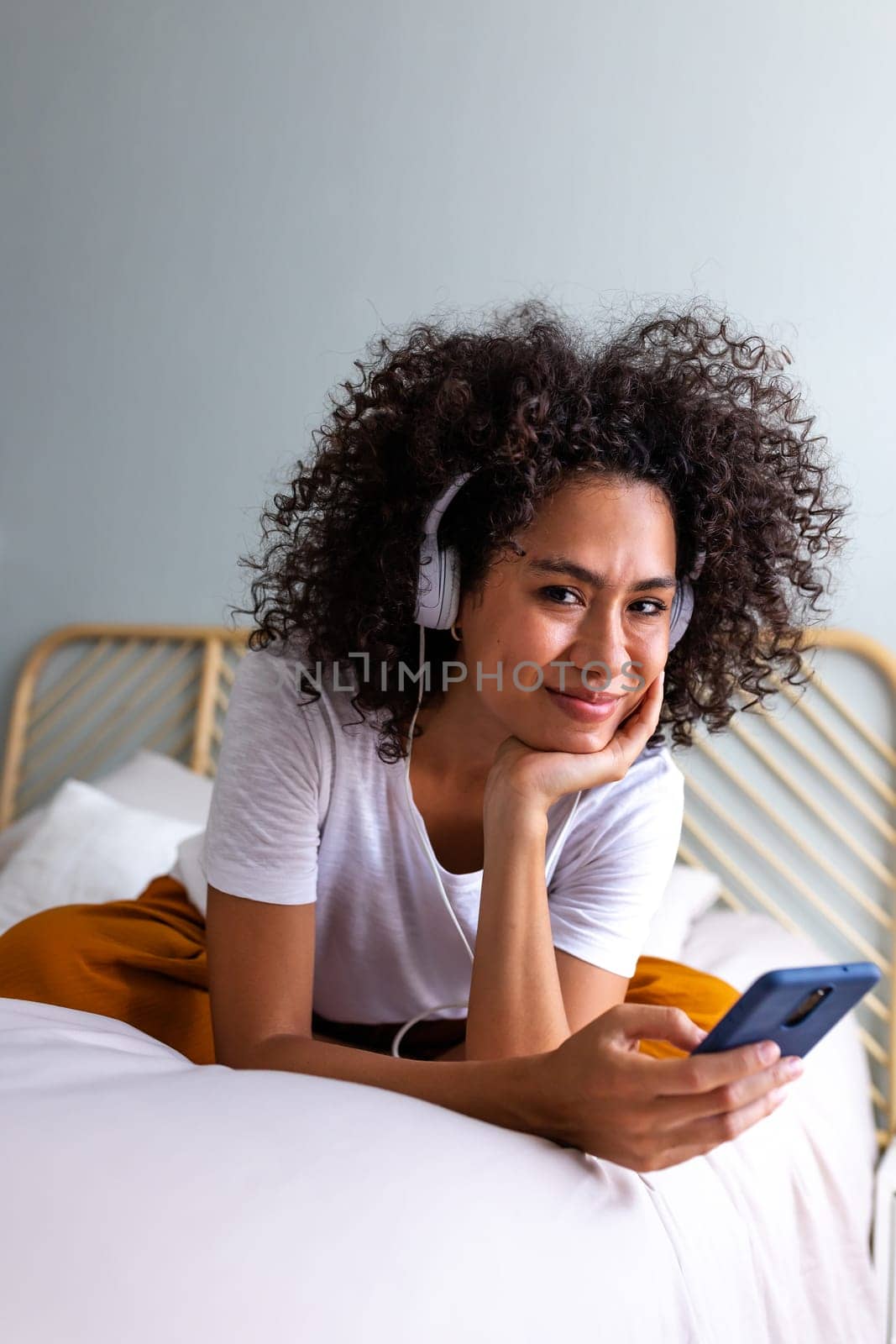 Happy young African American woman listening to music with headphones app mobile phone app looking at camera. by Hoverstock