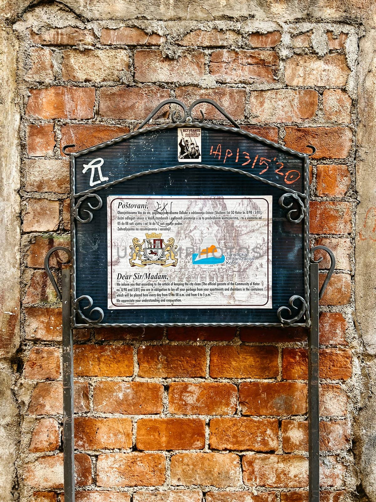 Forged signpost with coat of arms and text near an old brick wall. High quality photo