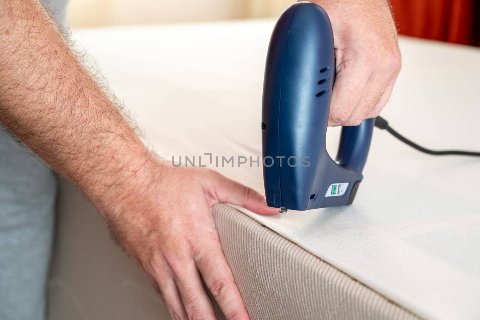 Worker stapling sofa lining with electric staple gun