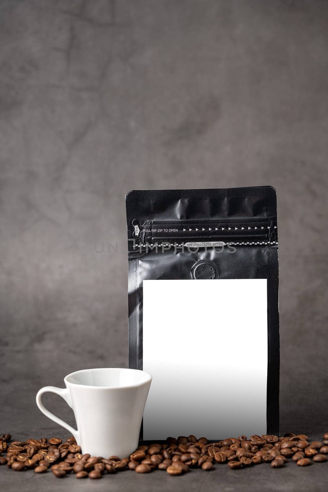 Black coffee foil packaging bag and coffee cup with blank white label on stone table by Sonat