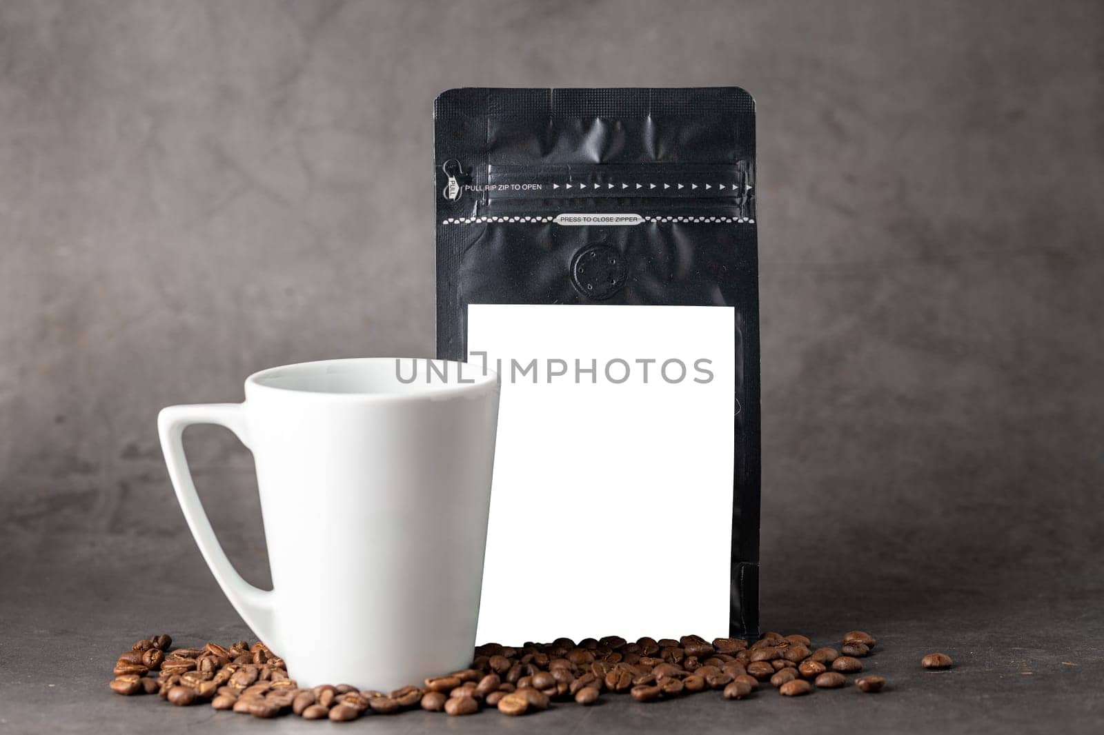 Black coffee foil packaging bag and coffee cup with blank white label on stone table by Sonat