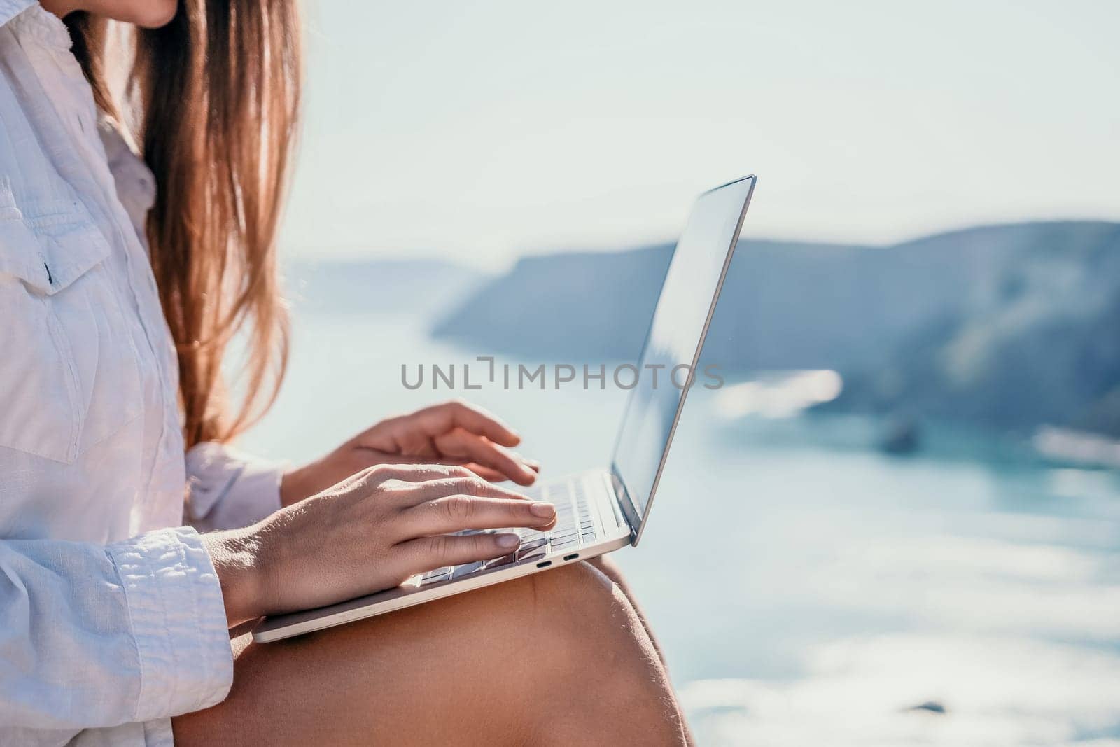 Woman sea laptop. Business woman in yellow hat freelancer with laptop working over blue sea beach. Girl relieves stress from work. Freelance, digital nomad, travel and holidays concept by panophotograph