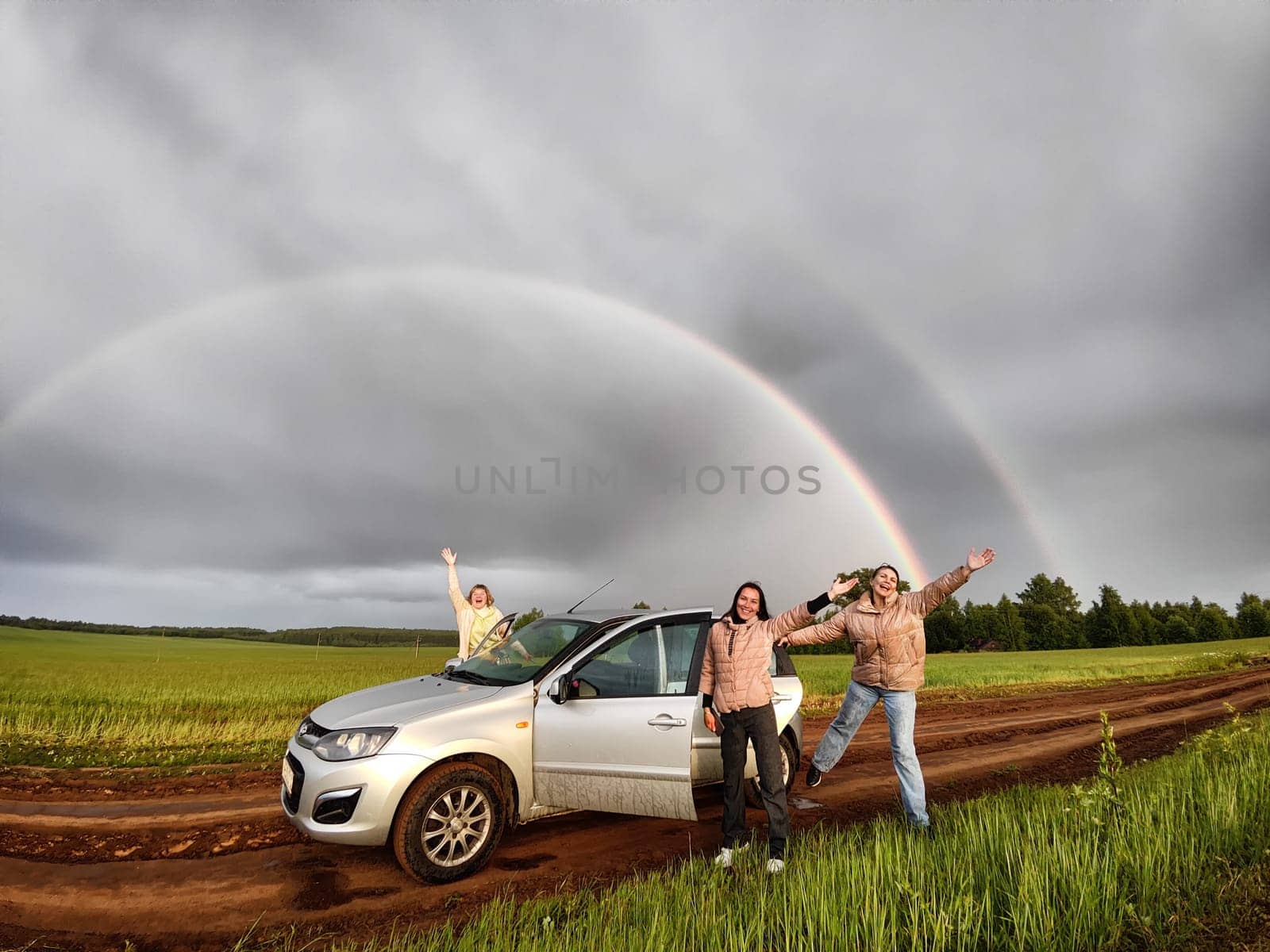 Three adult girl in a field with stormy sky with clouds and grey rainbow. A women having fun outdoors on rural and rustic nature near car. The Grey Rainbow and the Ban on LGBT symbols in Russia