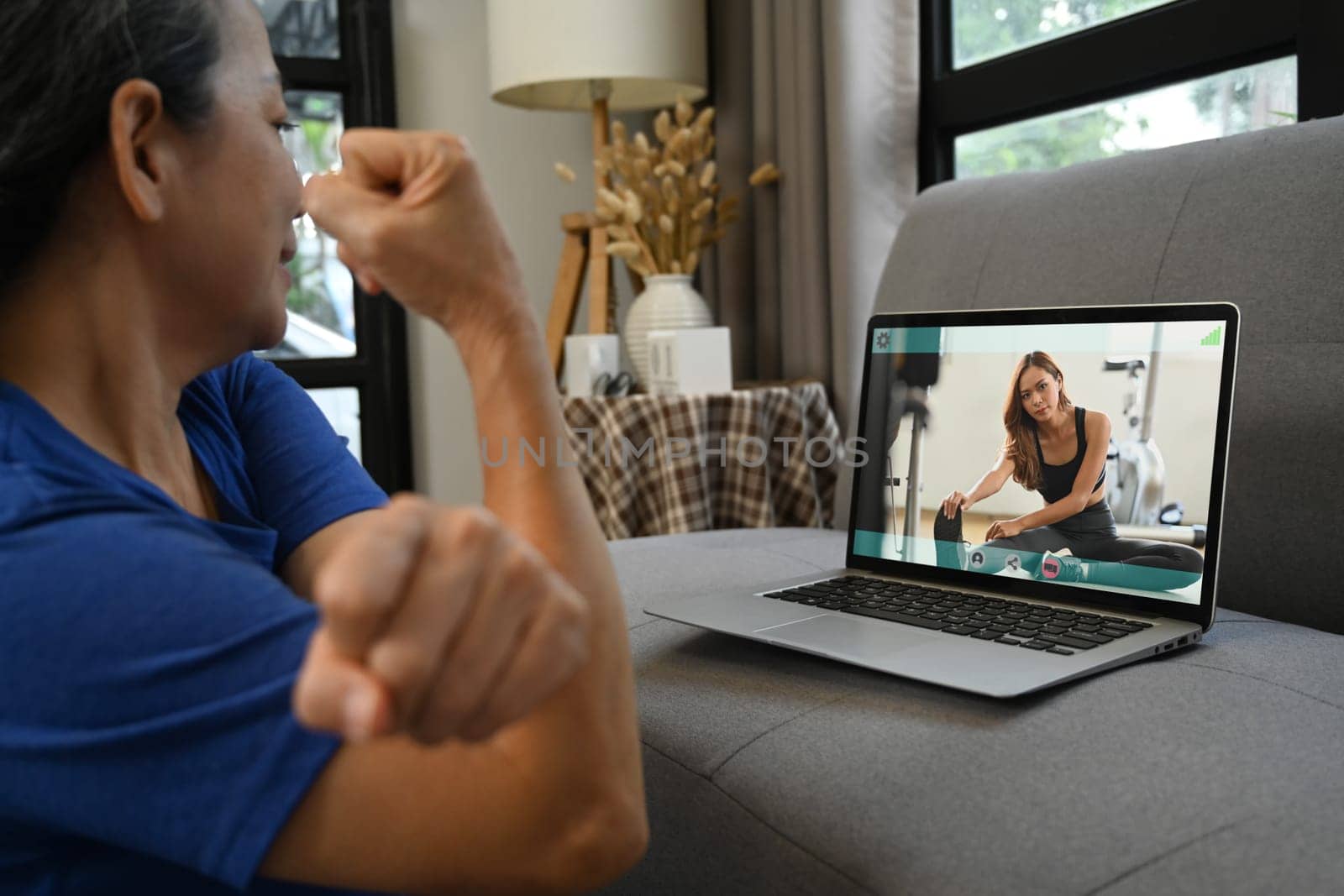 Cropped shot of senior woman exercising at home and watching tutorial training videos online on laptop. by prathanchorruangsak