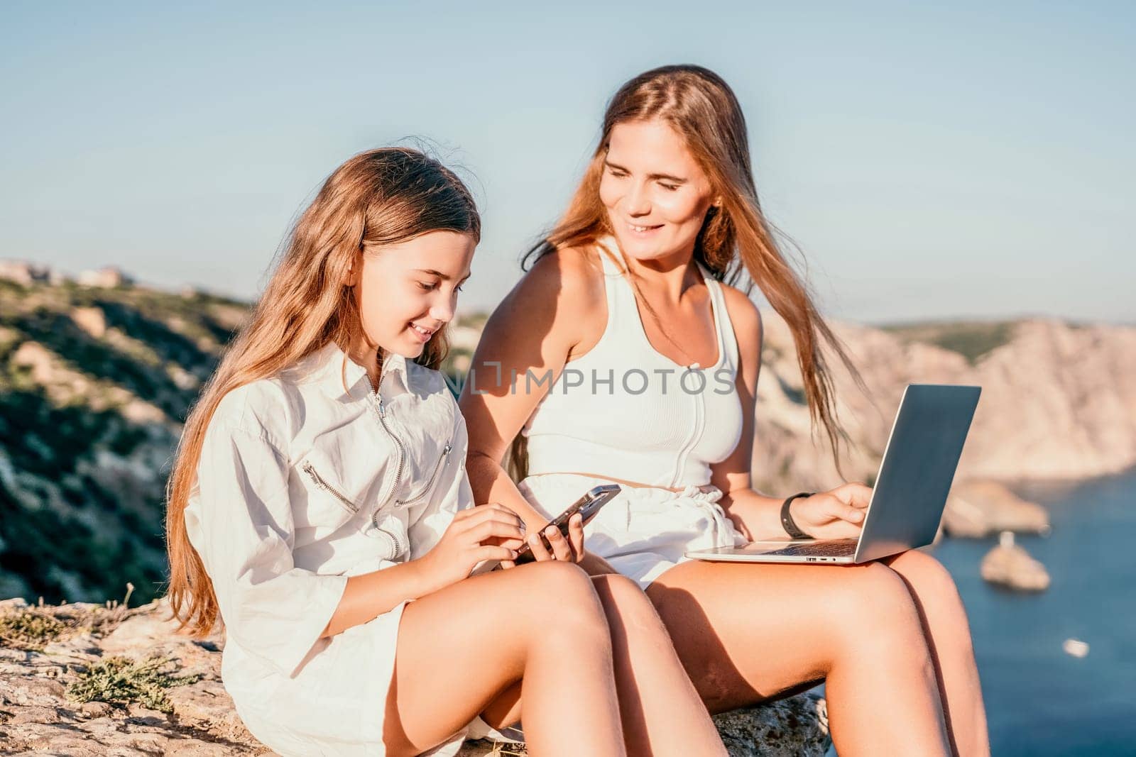 Successful business woman in yellow hat working on laptop by the sea. Pretty lady typing on computer at summer day outdoors. Freelance, travel and holidays concept.