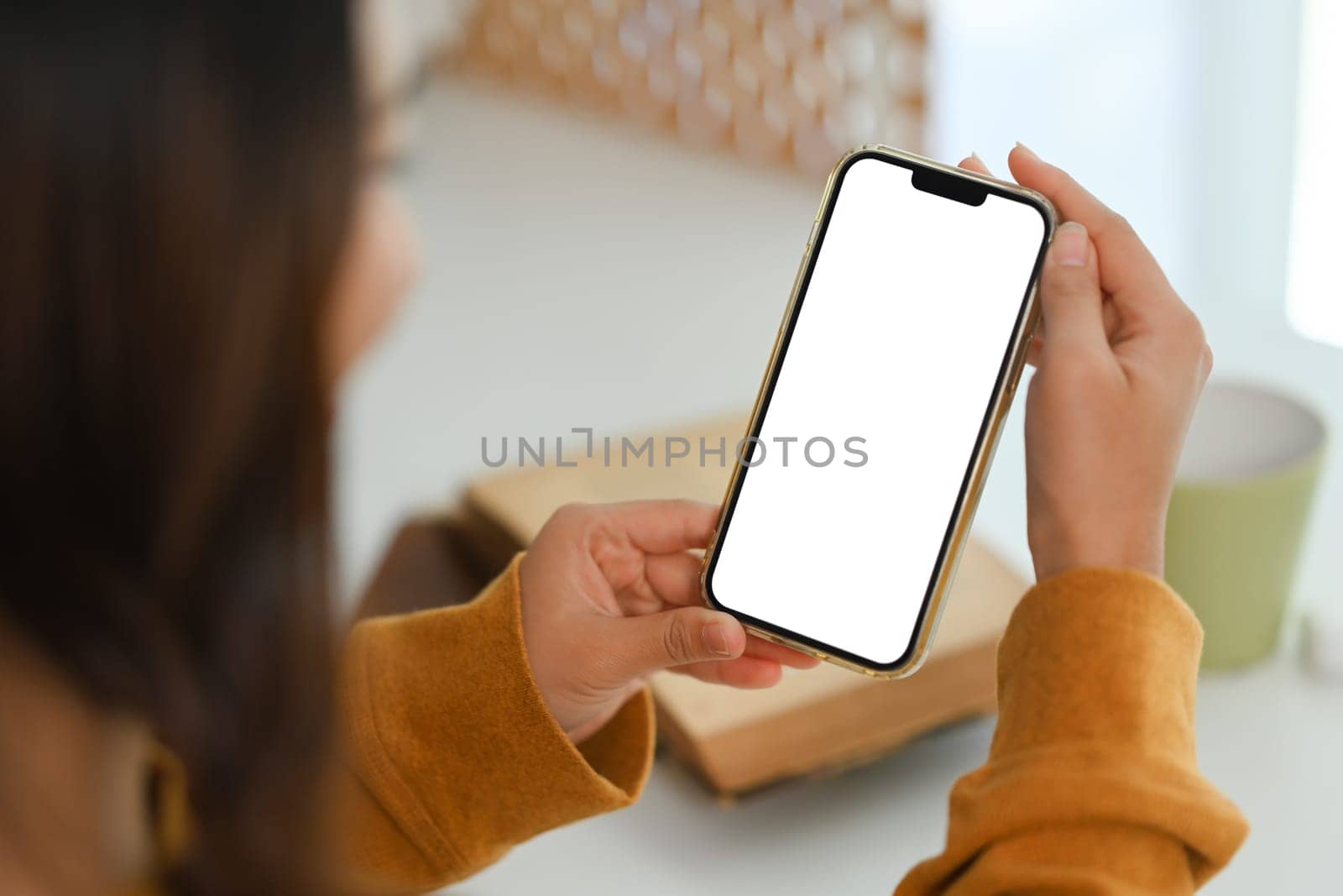 Over shoulder view woman holding mobile phone empty screen sitting at working desk. by prathanchorruangsak