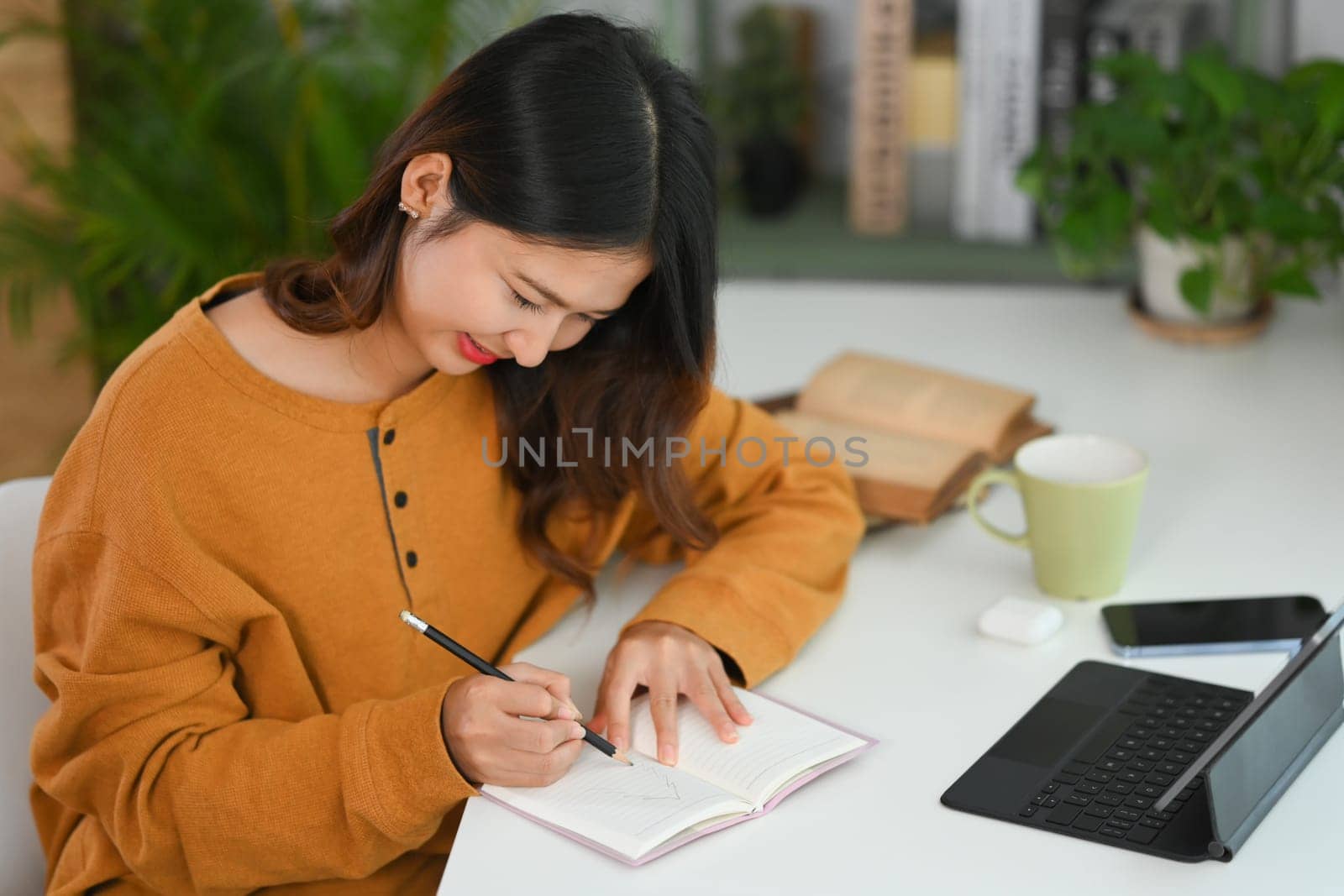 Pretty young Asian woman making important notes while planning daily appointment at her work desk