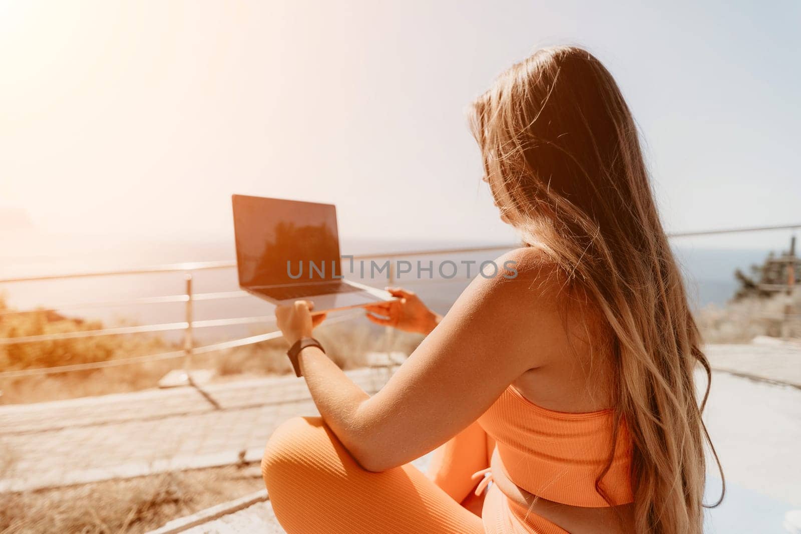 Woman laptop sea. Working remotely on seashore. Happy successful woman female freelancer working on laptop by the sea at sunset, makes a business transaction online. Freelance, remote work on vacation by panophotograph