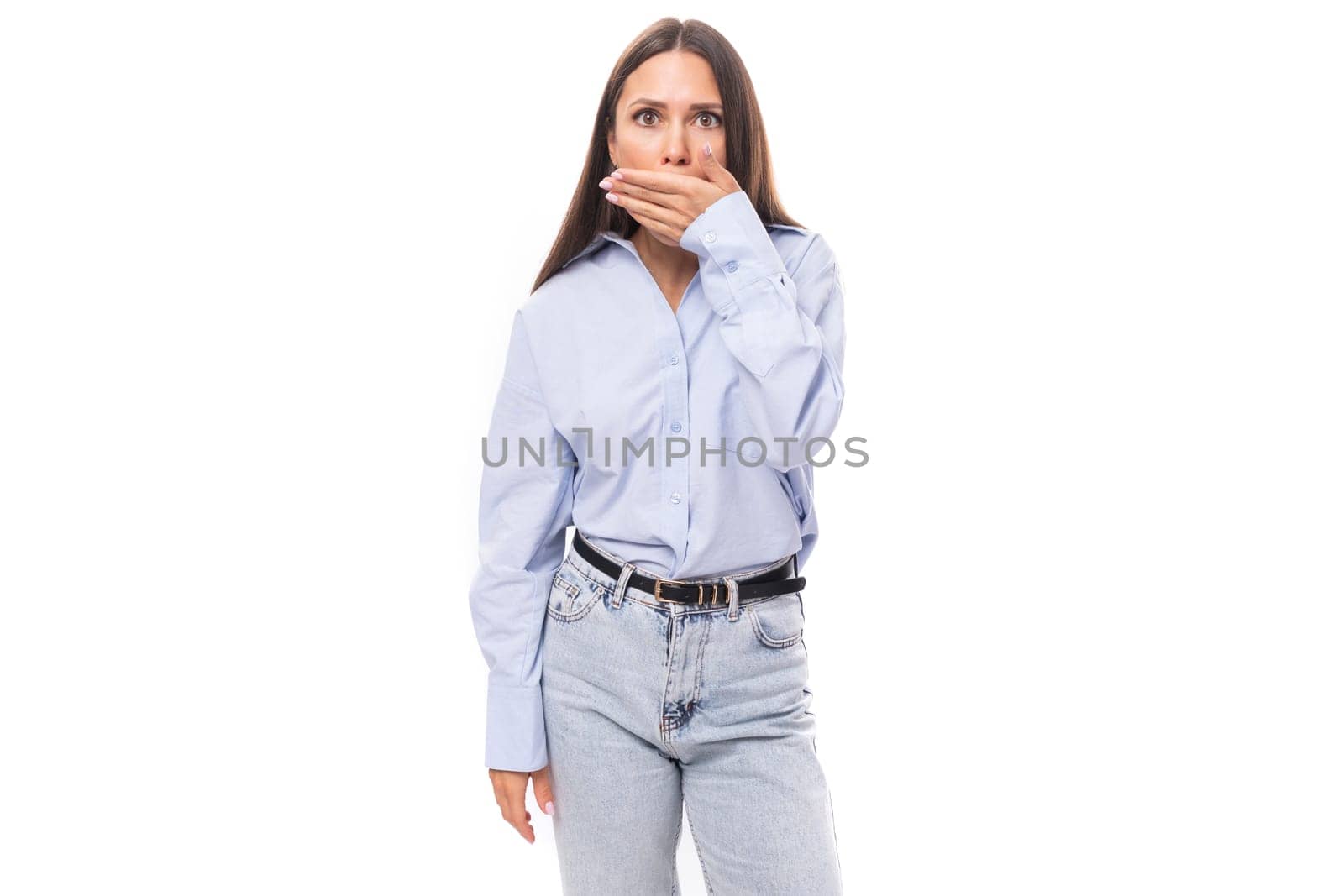 charming pretty young brunette caucasian woman with straight hair dressed in a sky blue shirt keeps a secret on a white background with copy space.