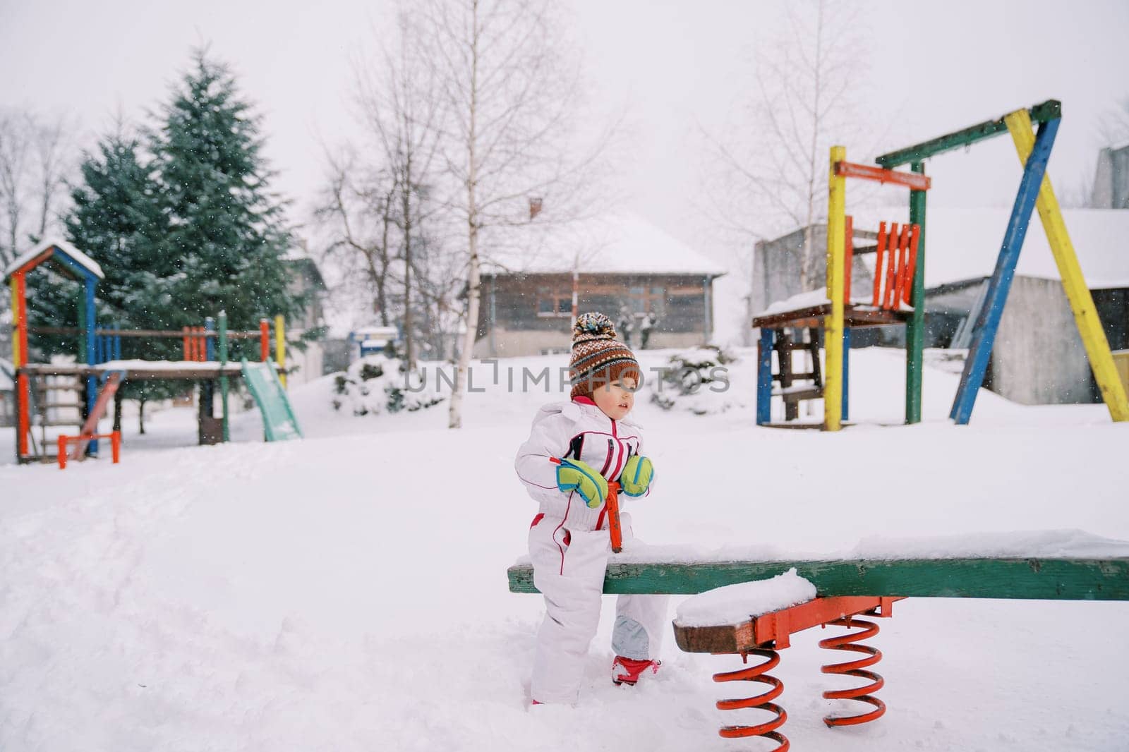 Little girl swing on a snow-covered swing-balancer at the playground. High quality photo