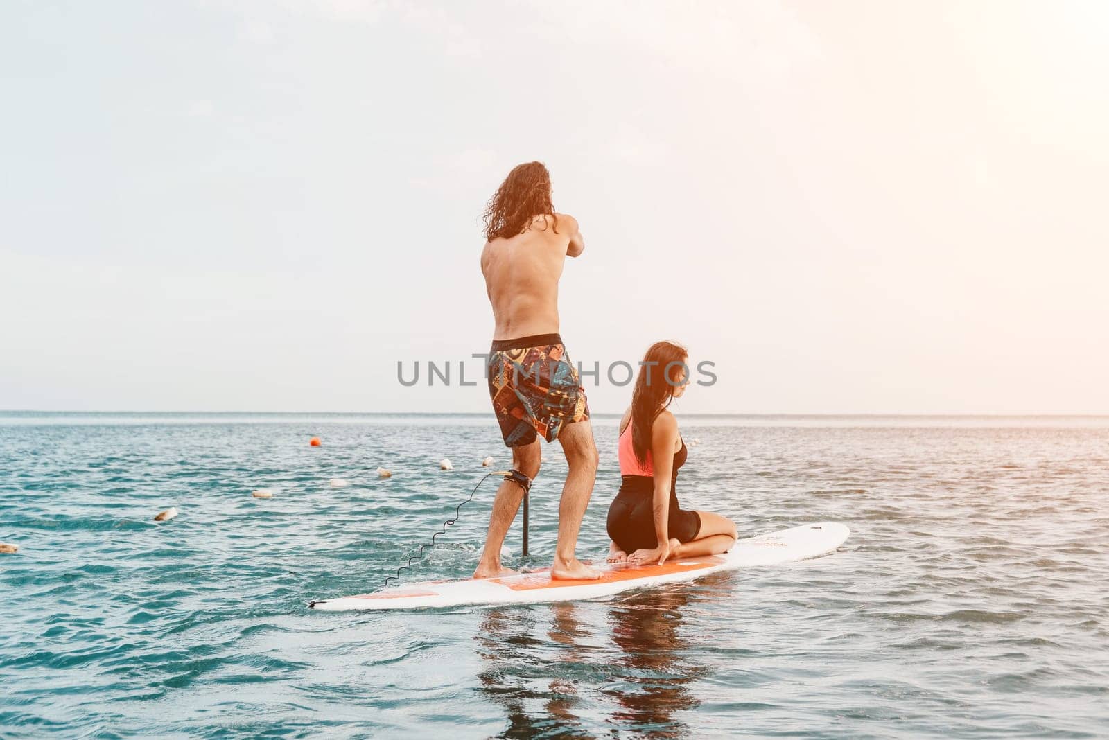 Sea woman and man on sup. Silhouette of happy young woman and man, surfing on SUP board, confident paddling through water surface. Idyllic sunset. Active lifestyle at sea or river. by panophotograph