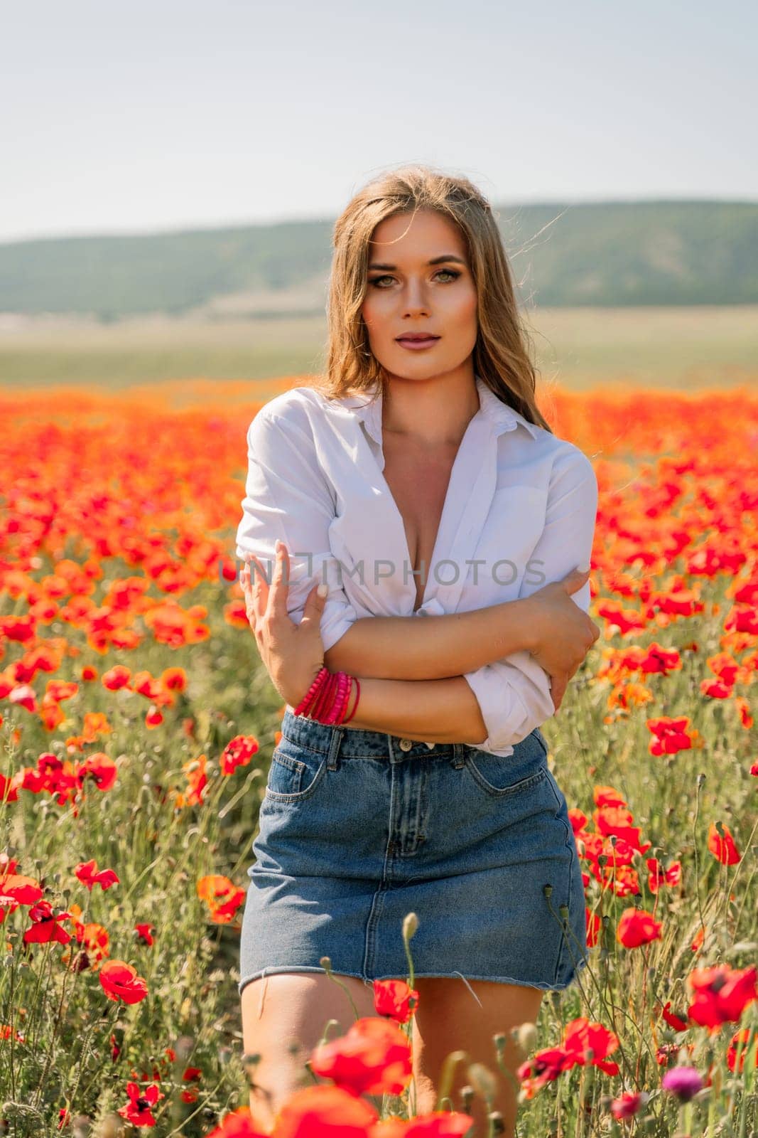 Happy woman in a poppy field in a white shirt and denim skirt with a wreath of poppies on her head posing and enjoying the poppy field. by Matiunina