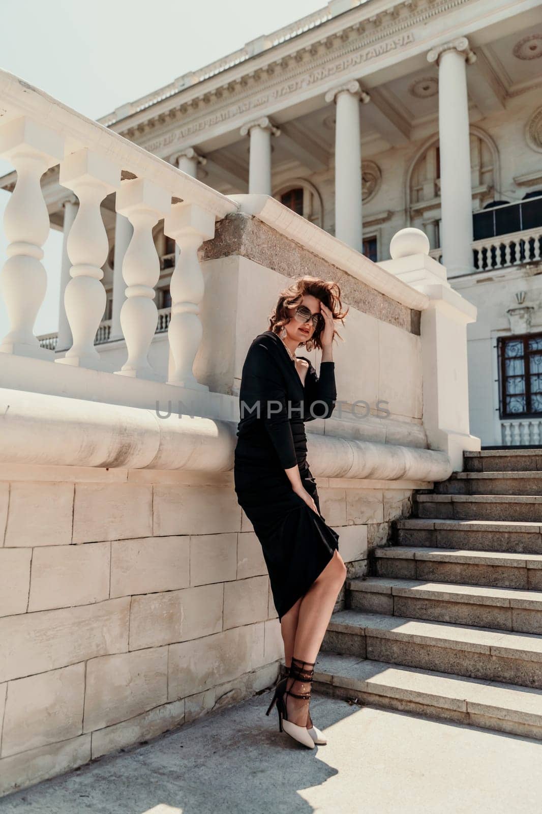 Stylish woman in the city. Fashion photo of a beautiful model in an elegant black dress posing against the backdrop of a building on a city street by Matiunina