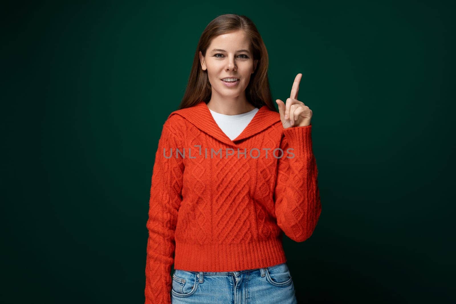 Well-groomed 30 year old woman with brown hair points her finger up.