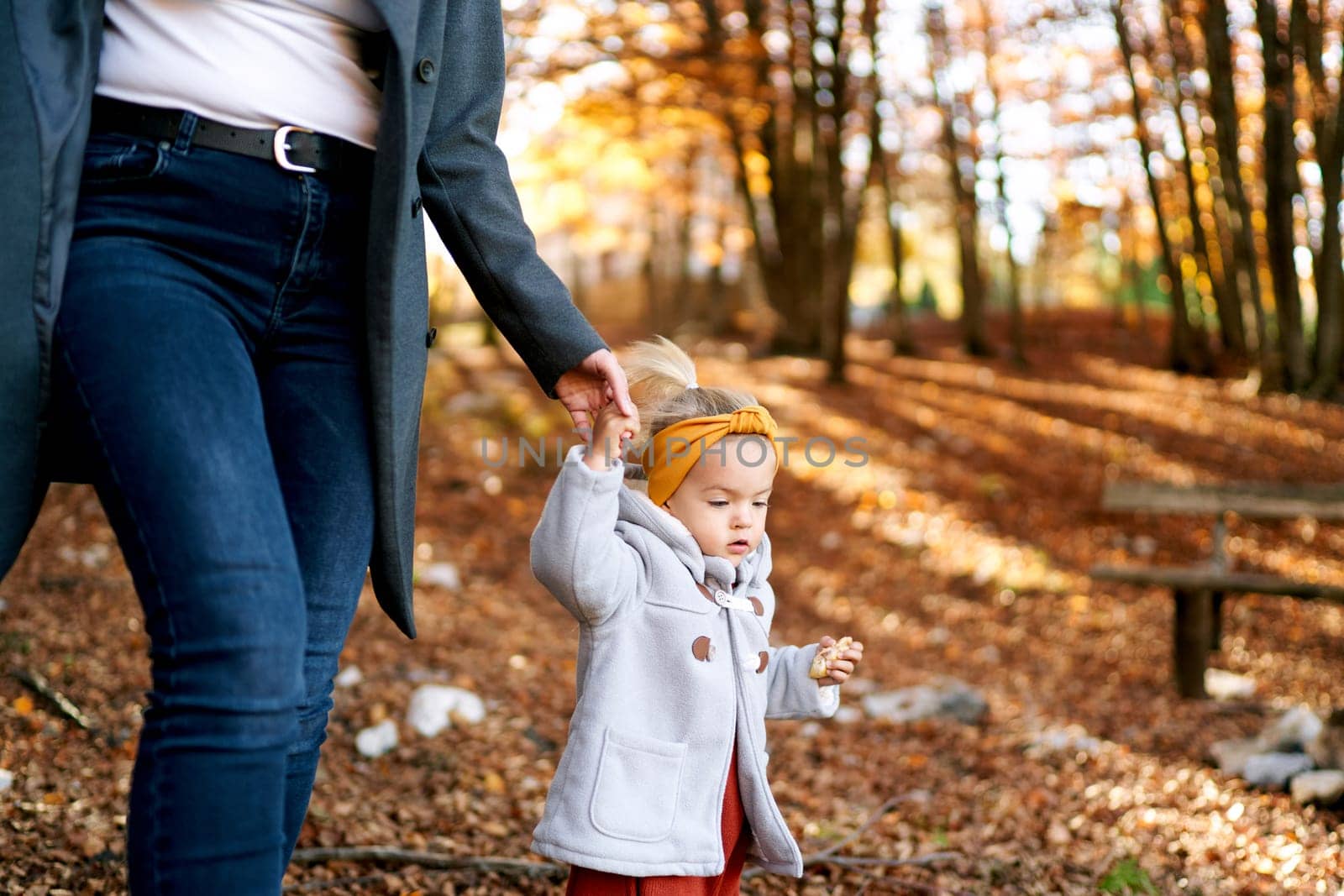 Mom leads a little girl through the park, holding her hand. Cropped by Nadtochiy