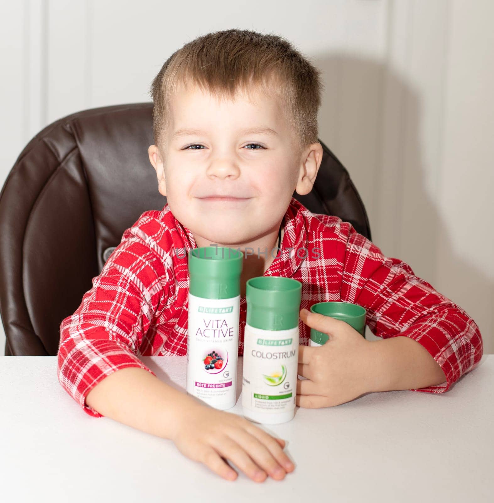 Dnepr, Ukraine - January 03,2024: a small handsome boy is sitting at a table with products from the cosmetic company LR Health and Beauty, vitamins, probiotic, colostrum. Close-up