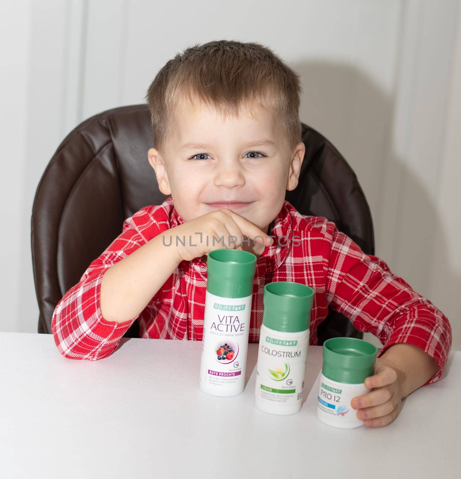 Dnepr, Ukraine - January 03,2024: a small handsome boy is sitting at a table with products from the cosmetic company LR Health and Beauty, vitamins, probiotic, colostrum. Close-up