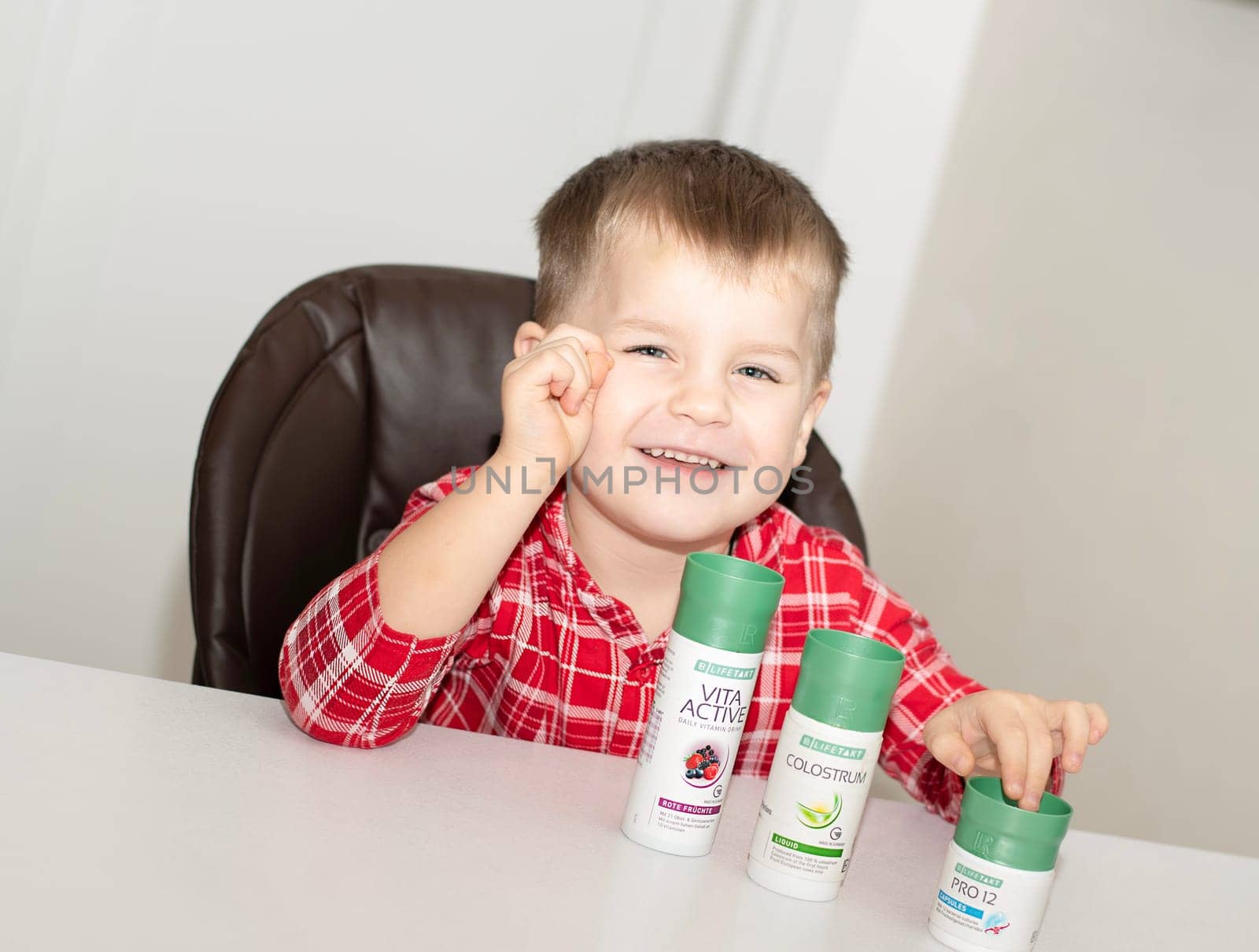 Dnepr, Ukraine - January 03,2024: a small handsome boy is sitting at a table with products from the cosmetic company LR Health and Beauty, vitamins, probiotic, colostrum. Close-up