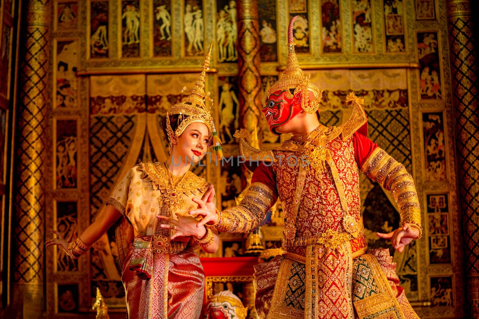 Beautiful Asian woman wear Thai traditional dress action of dancing together with Thai classic masked from the Ramakien character with Thai painting on public place wall.