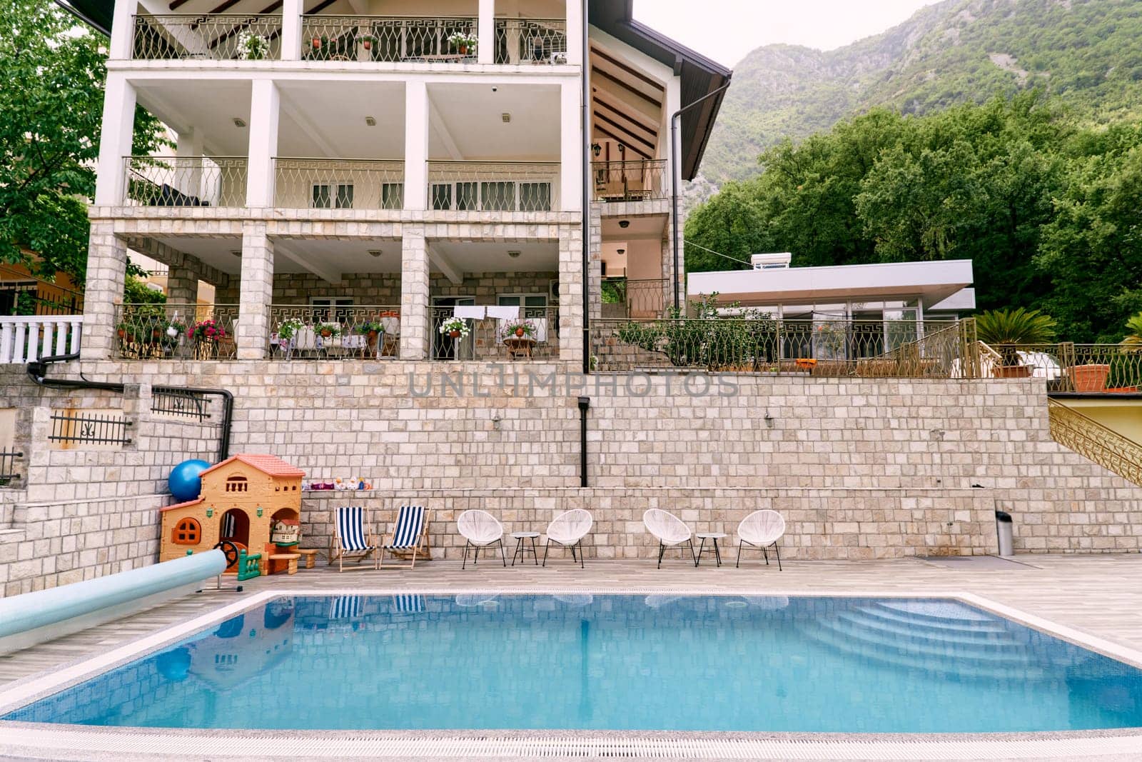 Wicker chairs with tables stand in front of the pool near a private hotel. High quality photo