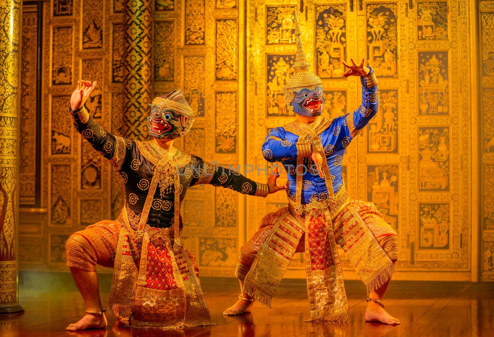 Khon or traditional Thai classic masked from the Ramakien with black and blue monkey stand together with action of traditional dance with Thai paintings background in a public place.