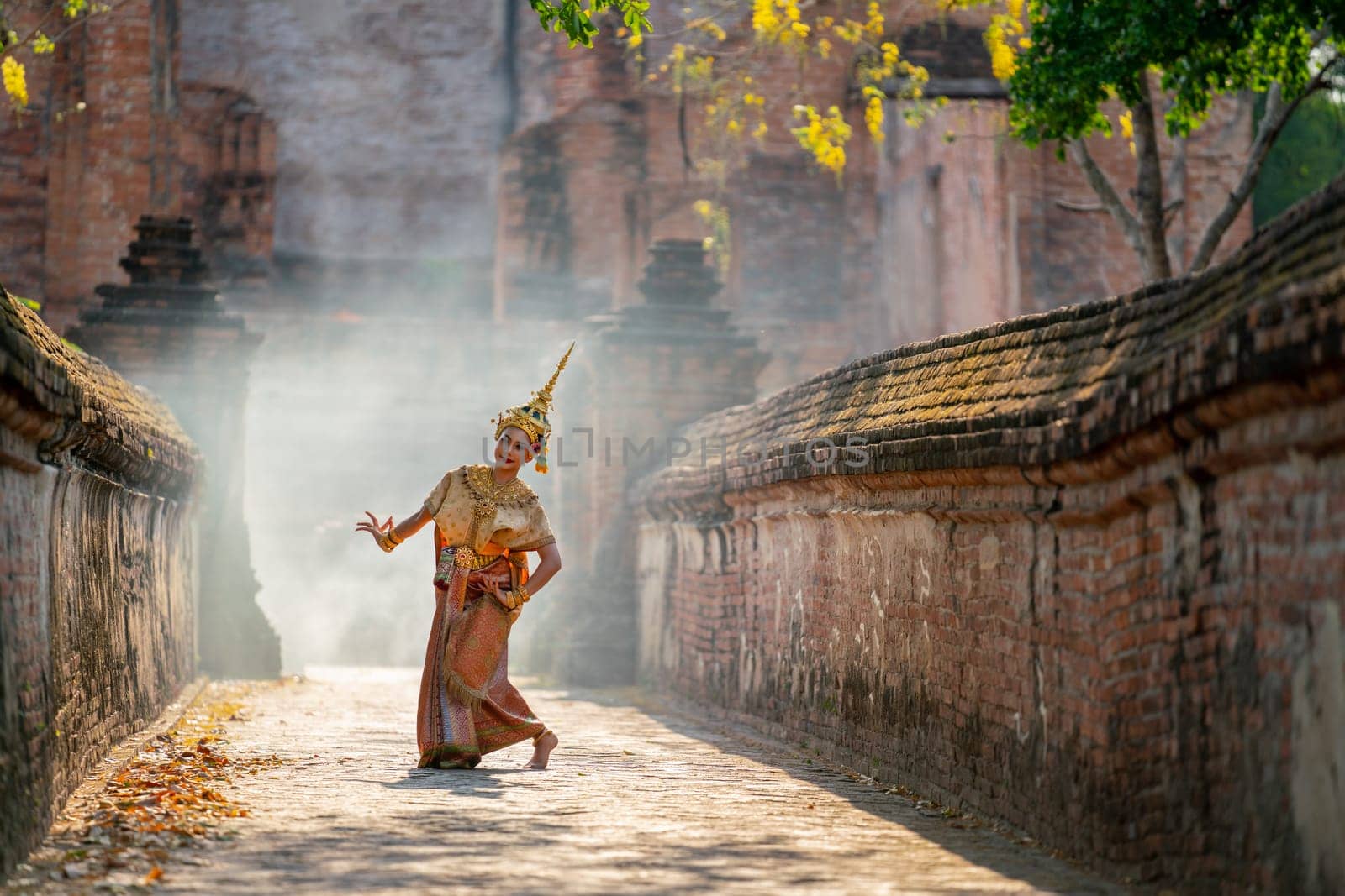 Asian beautiful woman with traditional dress dance with different actions on the way to ancient building and smoke or mist in the background with day light.