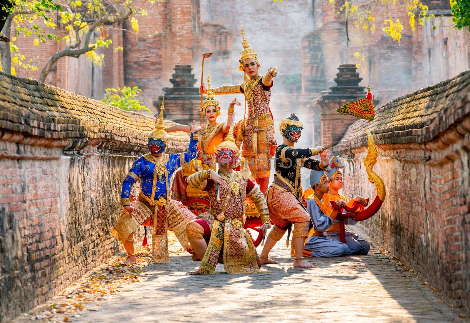 Small group of Khon or traditional Thai classic masked from the Ramakien characters stand together with action of traditional dance with Thai ancient building in background.