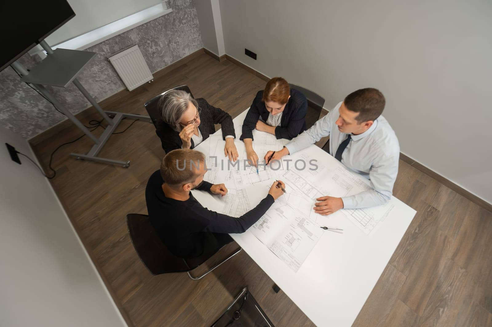 Top view of 4 business people sitting at a table and discussing blueprints. Designers engineers at a meeting