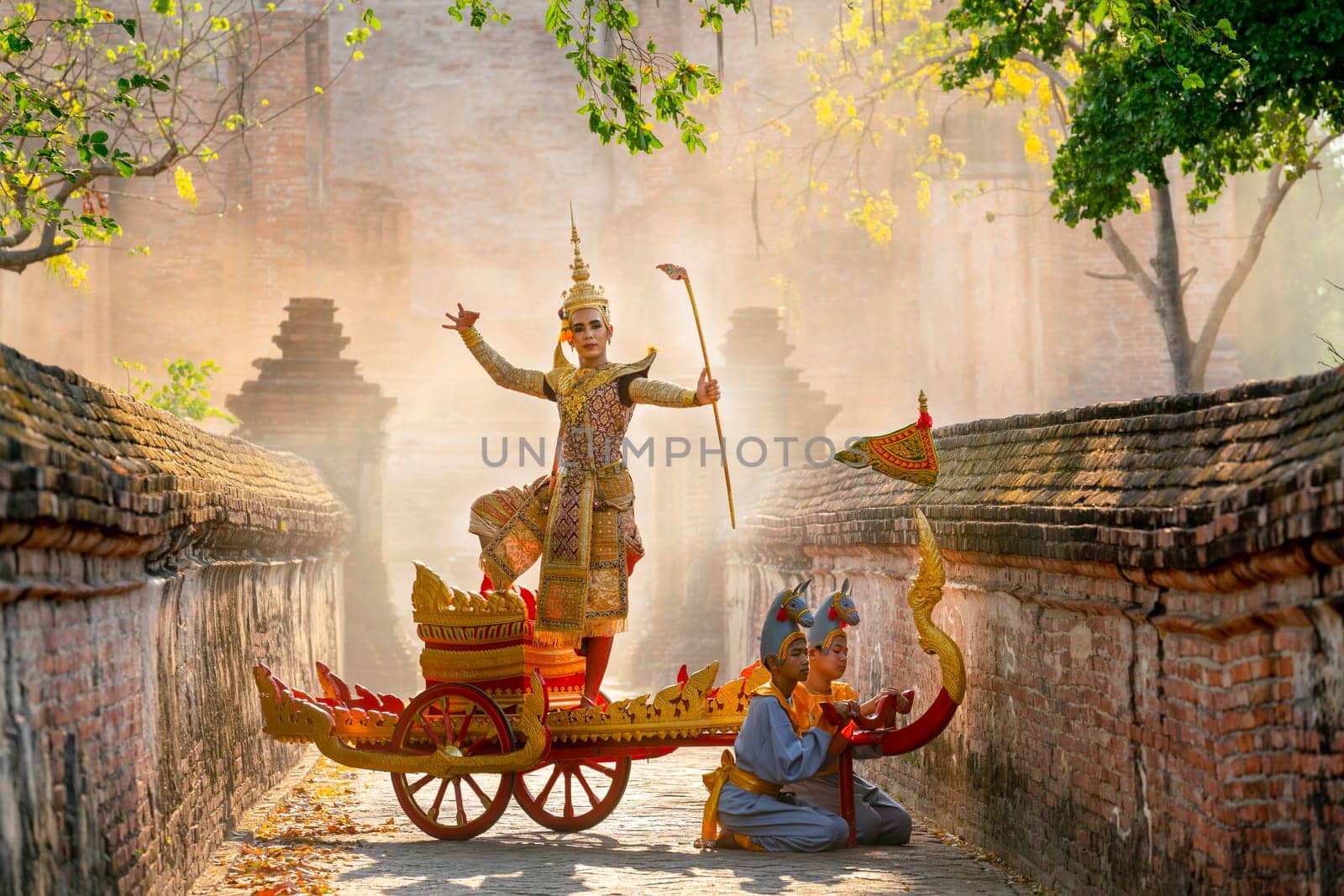 Asian man with old Thai traditional cloth hold weapon and stand and action of dance on traditional chariot also hold weapon stay in front of ancient building.